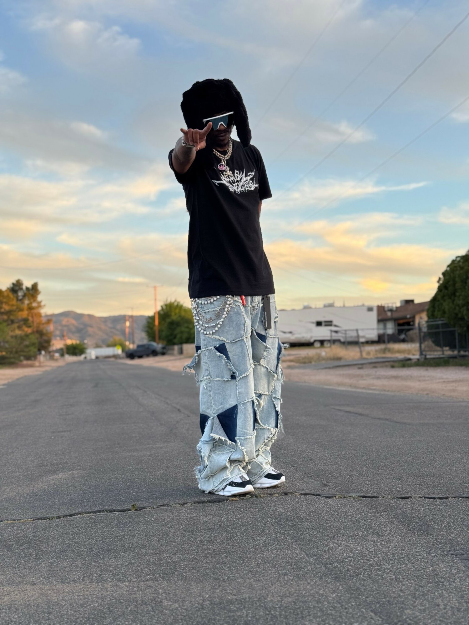 Person standing in the middle of an empty street, pointing towards the camera, with a sky and buildings in the background.