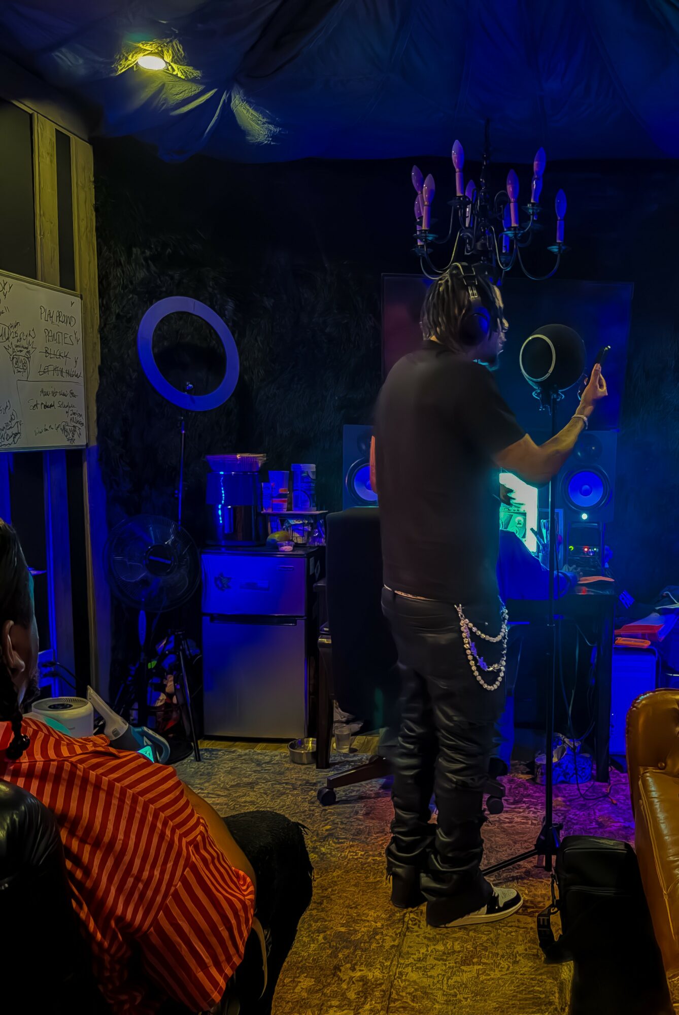 Person standing in a dimly lit room with a chandelier, writing on a board, surrounded by colorful furniture and decorations.