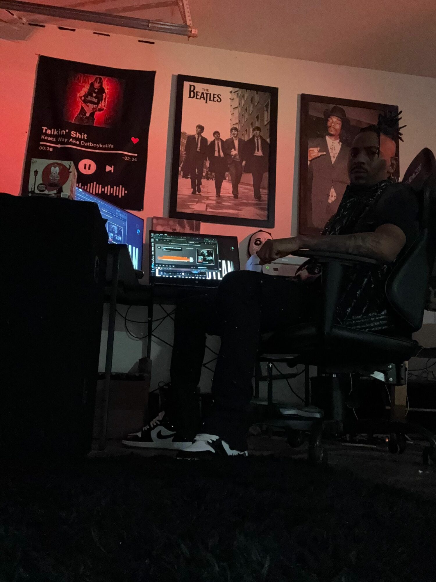 Person standing in front of DJ equipment and computer screens in a dimly lit room.