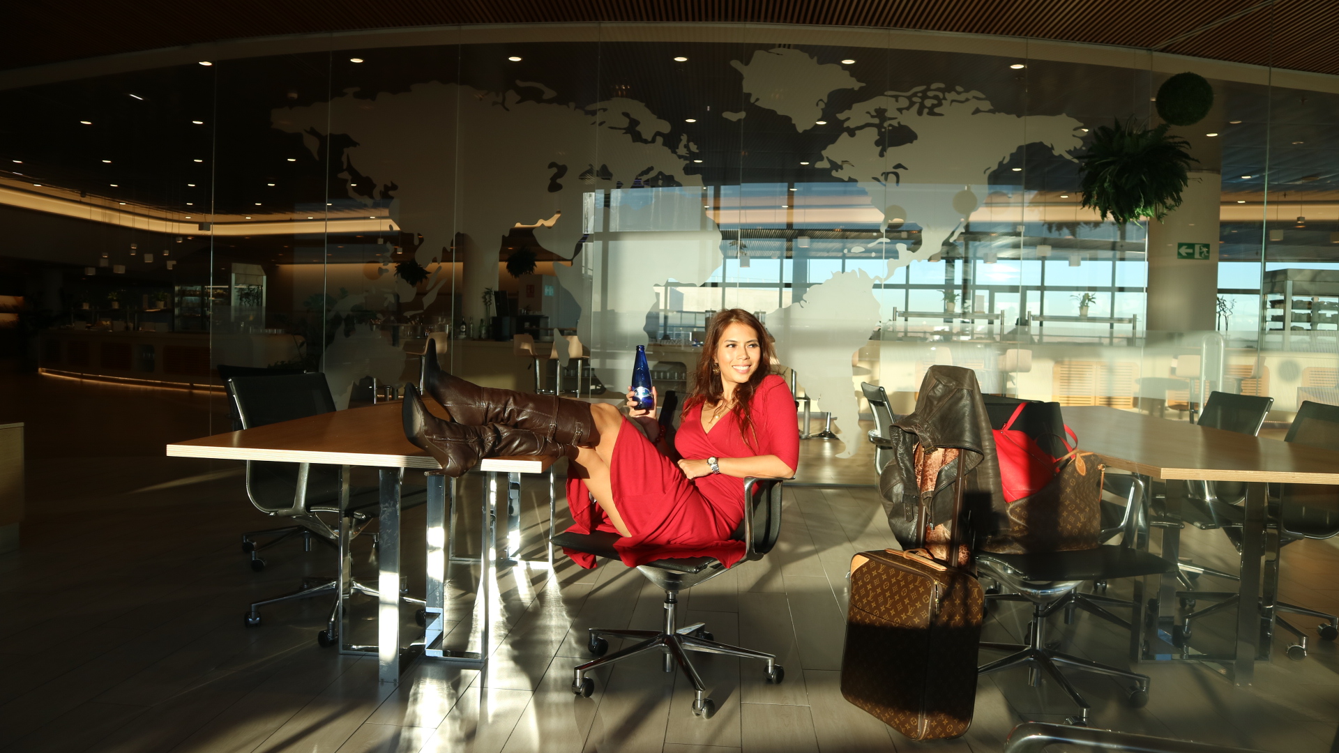 Woman in red dress sitting on a conference table in a modern office with glass walls and reflections.