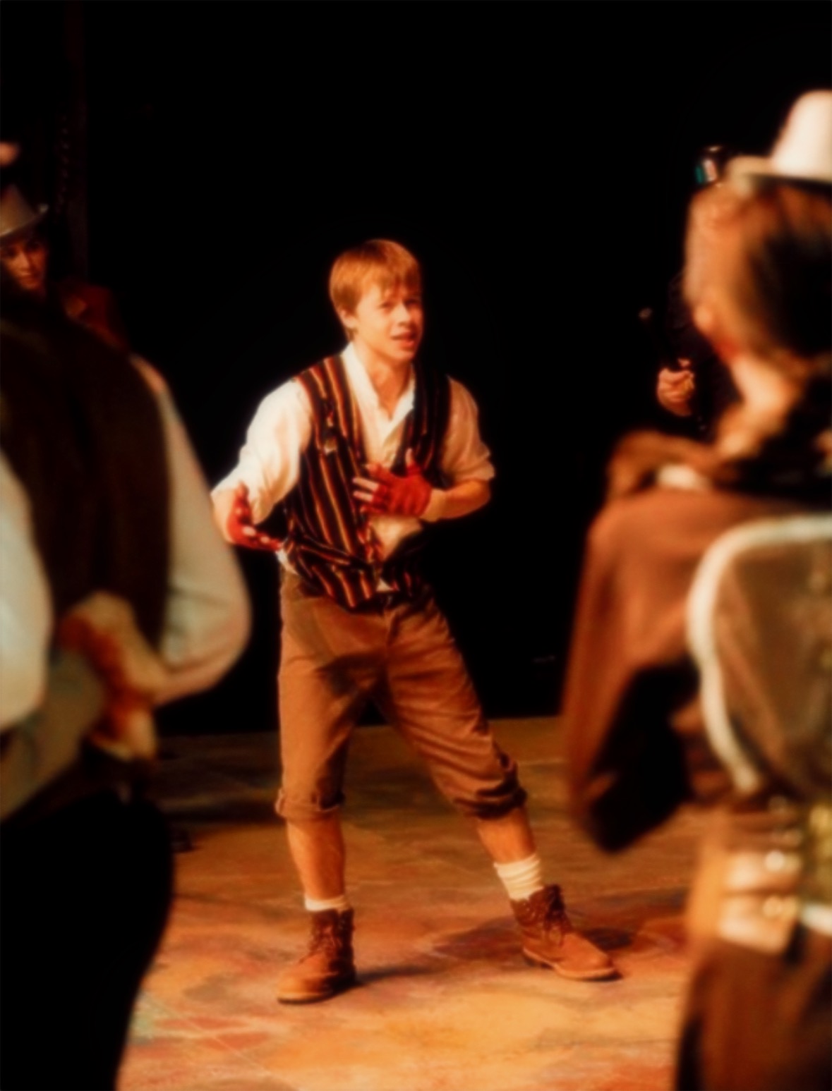 Young person performing on stage with others, wearing vintage-style clothing, in a theatrical setting.