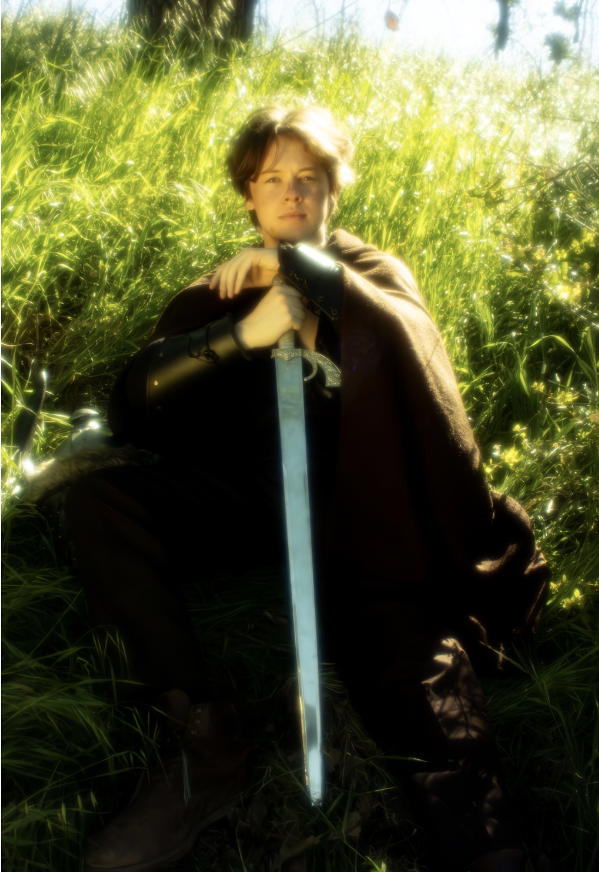 Person sitting outdoors with a sword, surrounded by green grass and sunlight, wearing dark clothing and gloves.