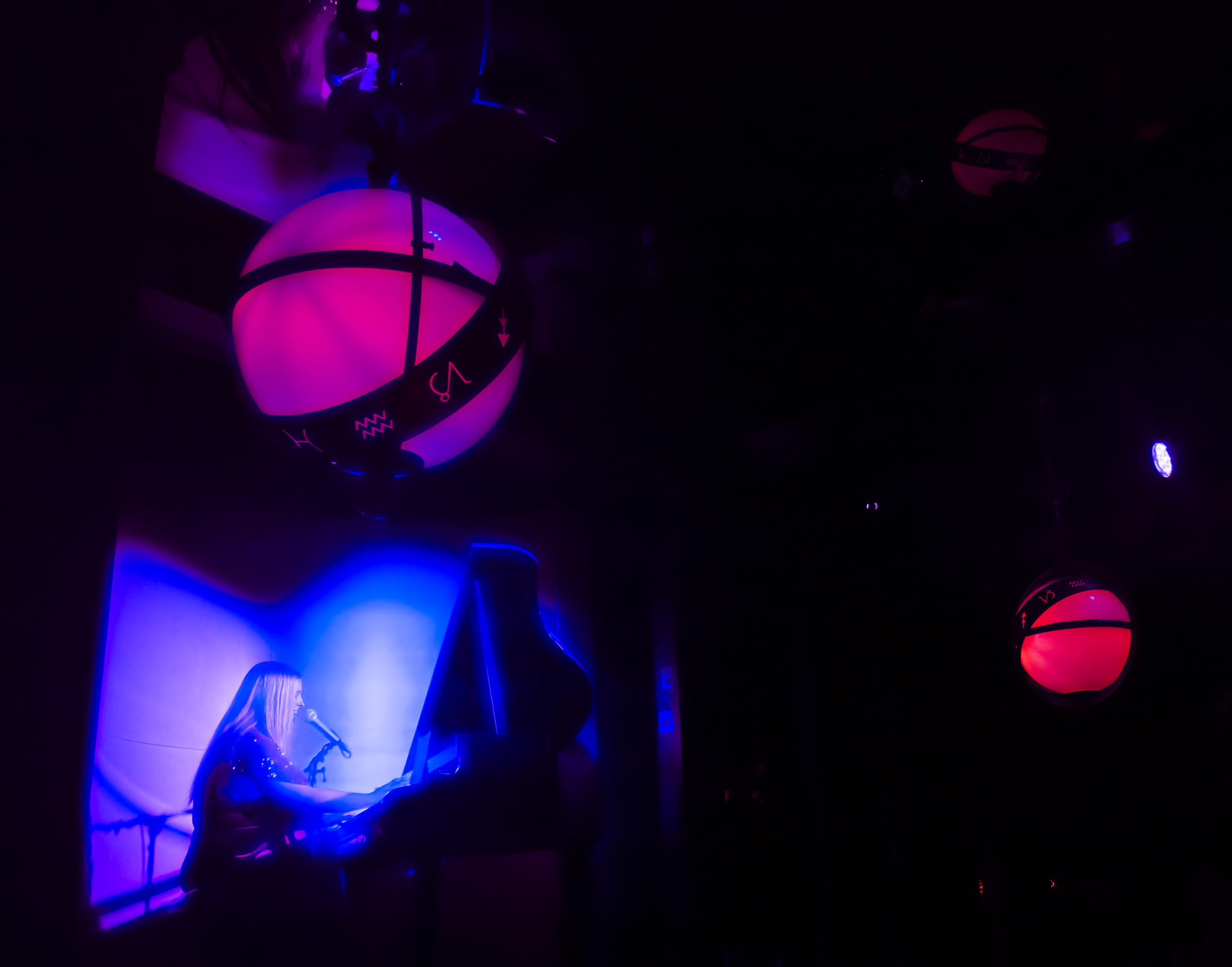 Person sitting on a chair in a dark room illuminated by purple and blue lights, with glowing spherical objects hanging from the ceiling.