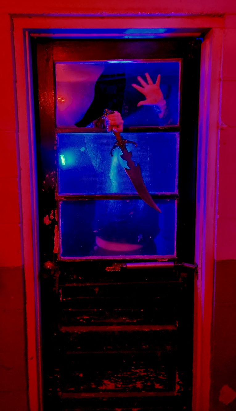 Person taking a mirror selfie with a hand reaching out, illuminated by colorful lights, in a window with multiple panes.
