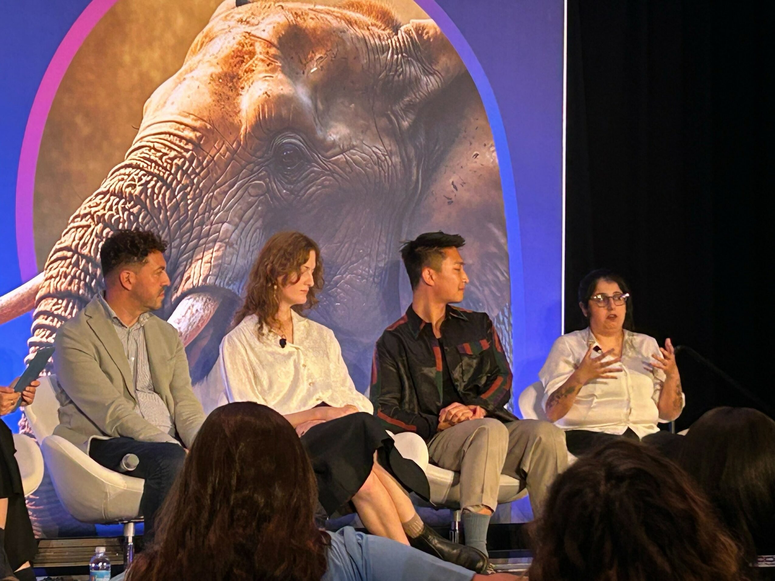 Four people sit on a stage in front of a large image of an elephant, engaging in a discussion.