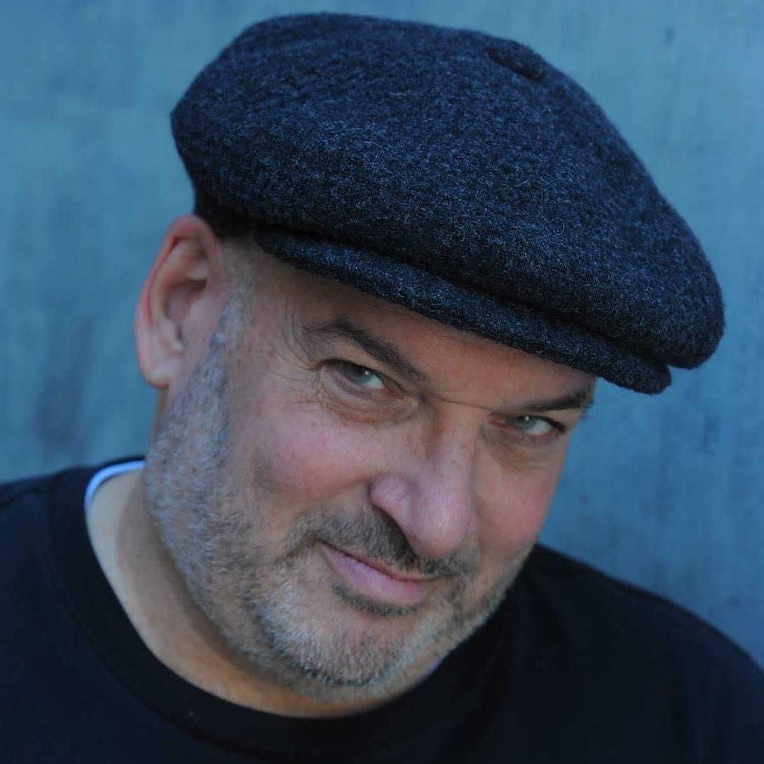 Man wearing a dark cap, smiling, with a blue background.