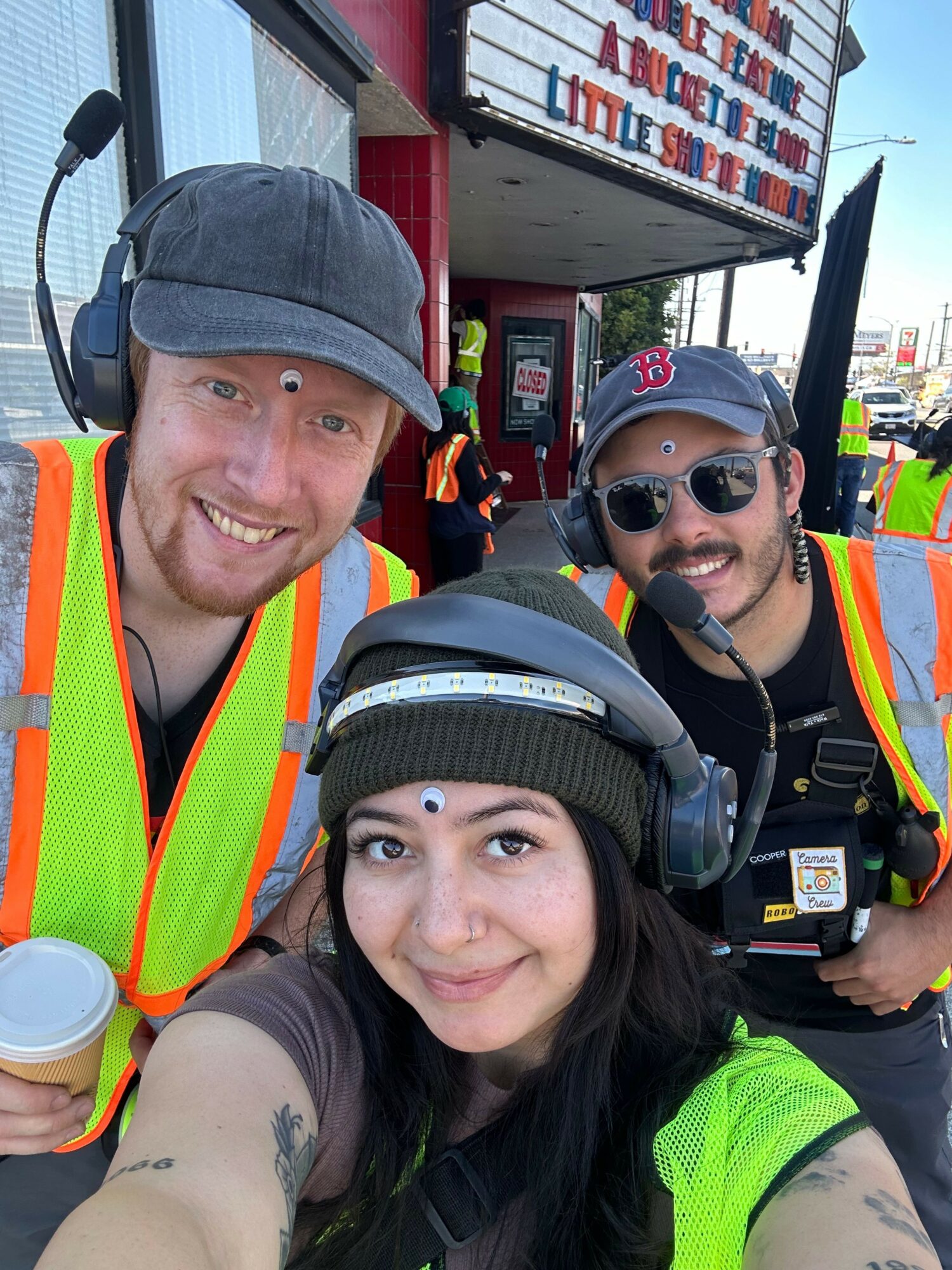 Three people wearing safety vests and helmets taking a selfie outdoors, smiling and looking at the camera.