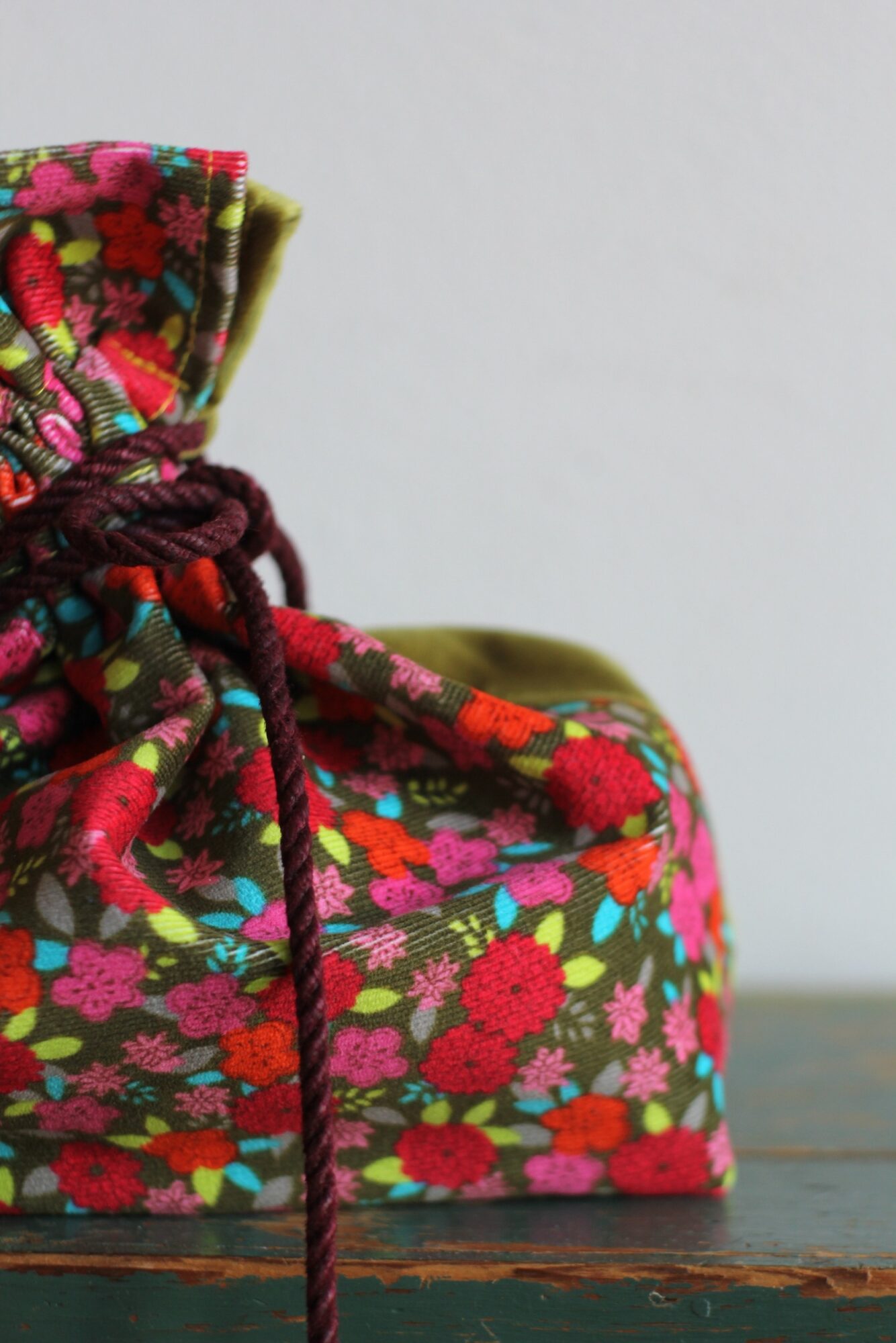 Close-up of a colorful floral fabric bag with a drawstring, placed on a wooden surface against a plain background.