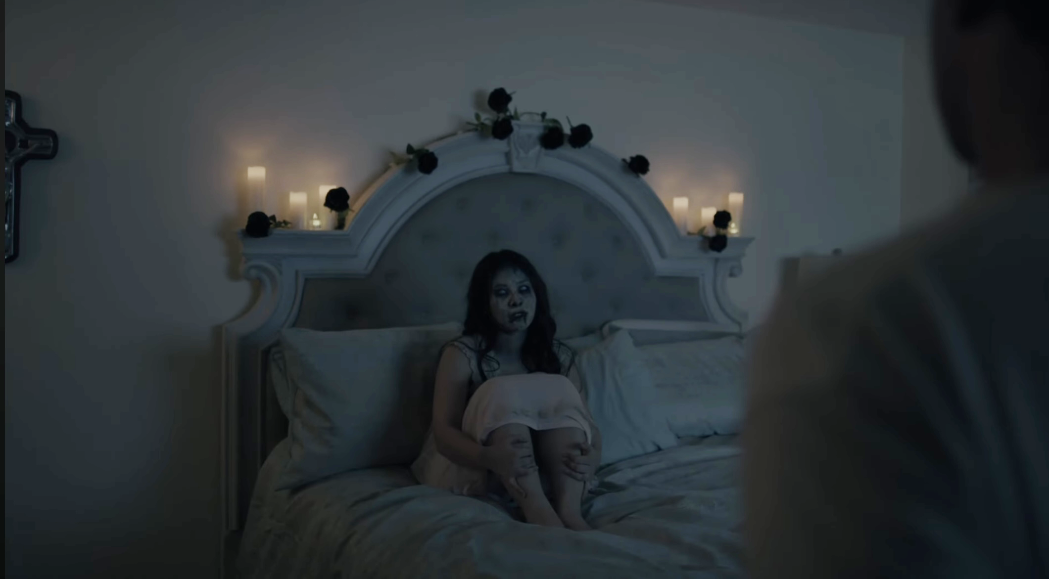 Person sitting on a bed in a dimly lit room with candles and decorative items on the headboard.