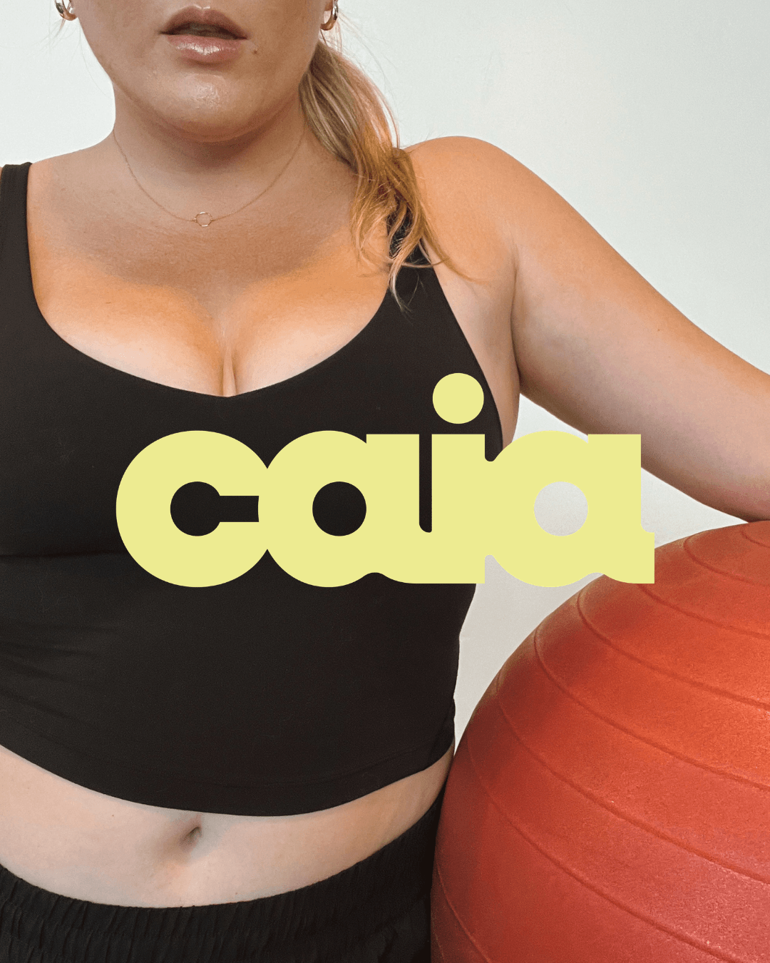 Woman in black sports bra holding an orange exercise ball, with text overlay reading 'cai'.