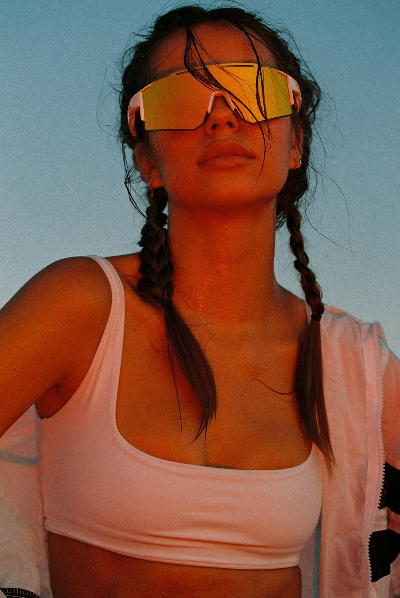 Woman with braided hair wearing reflective sunglasses and a white tank top outdoors.