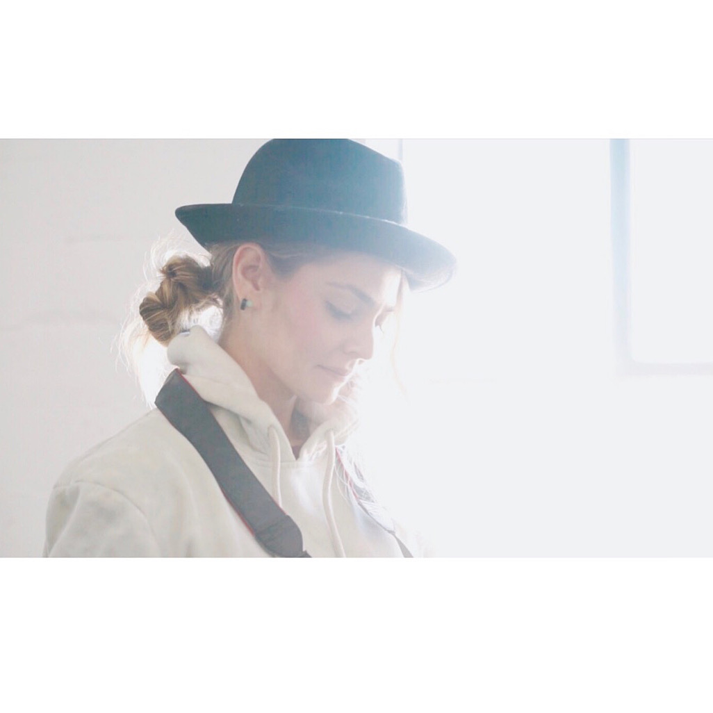 Woman wearing a hat and coat, looking down, with light coming from a window on the right side.
