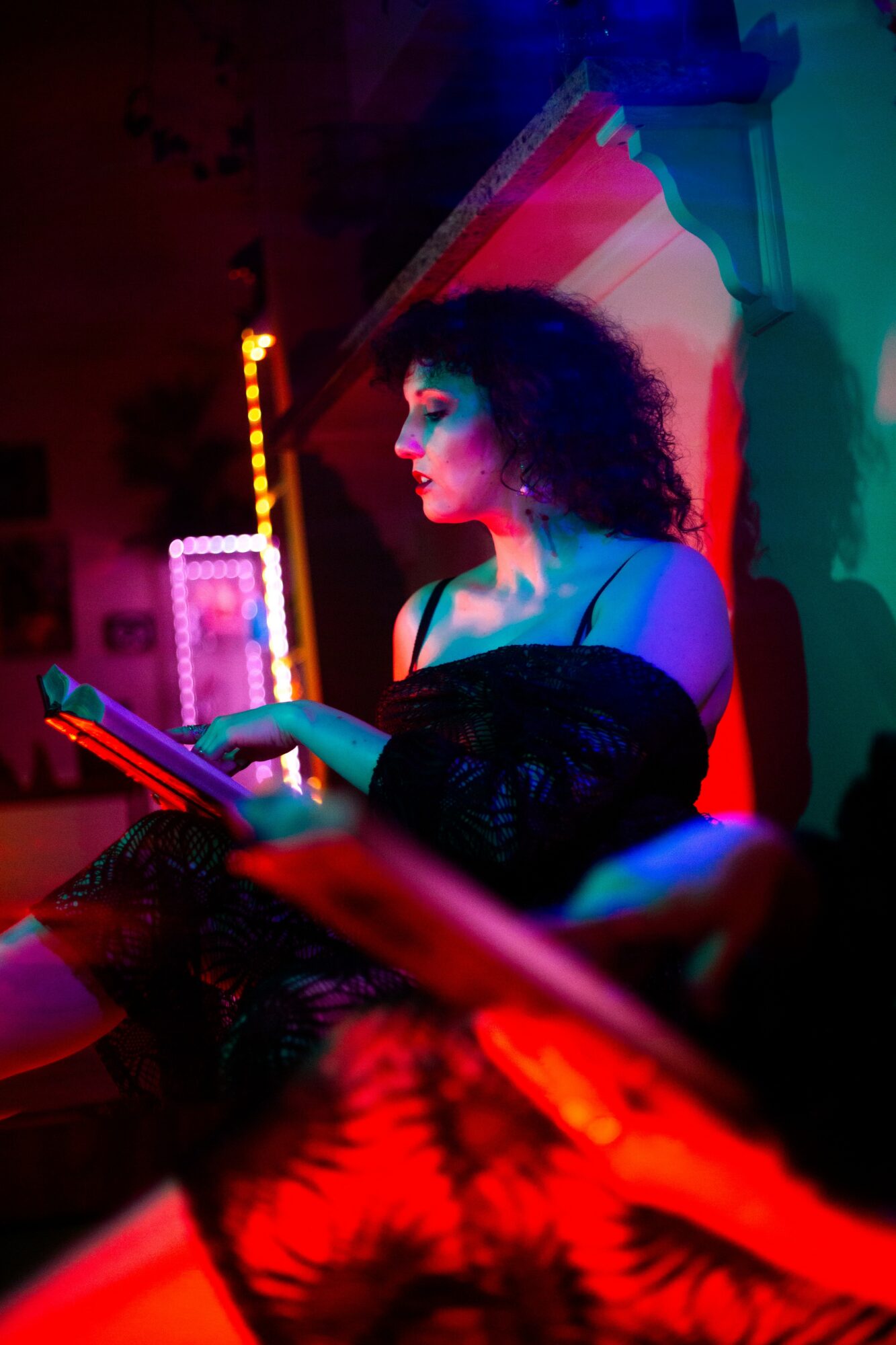 Woman with curly hair reading a book in colorful neon-lit environment.