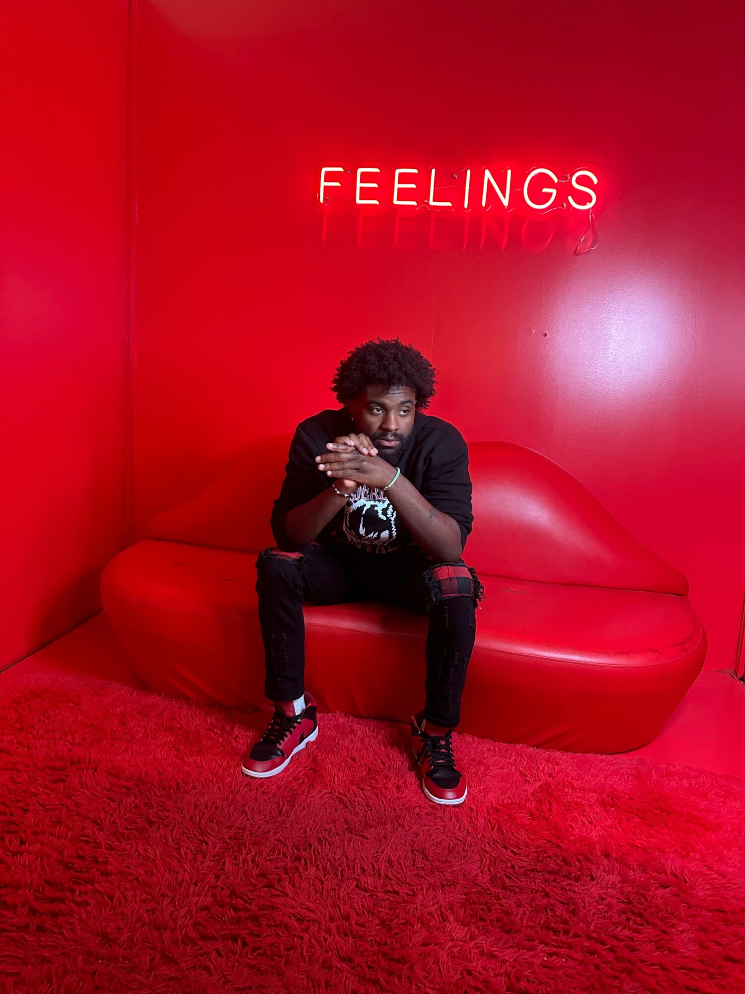 Person sitting on a red couch in a room with red walls and carpet, holding a phone, with the word FEELINGS on the wall.