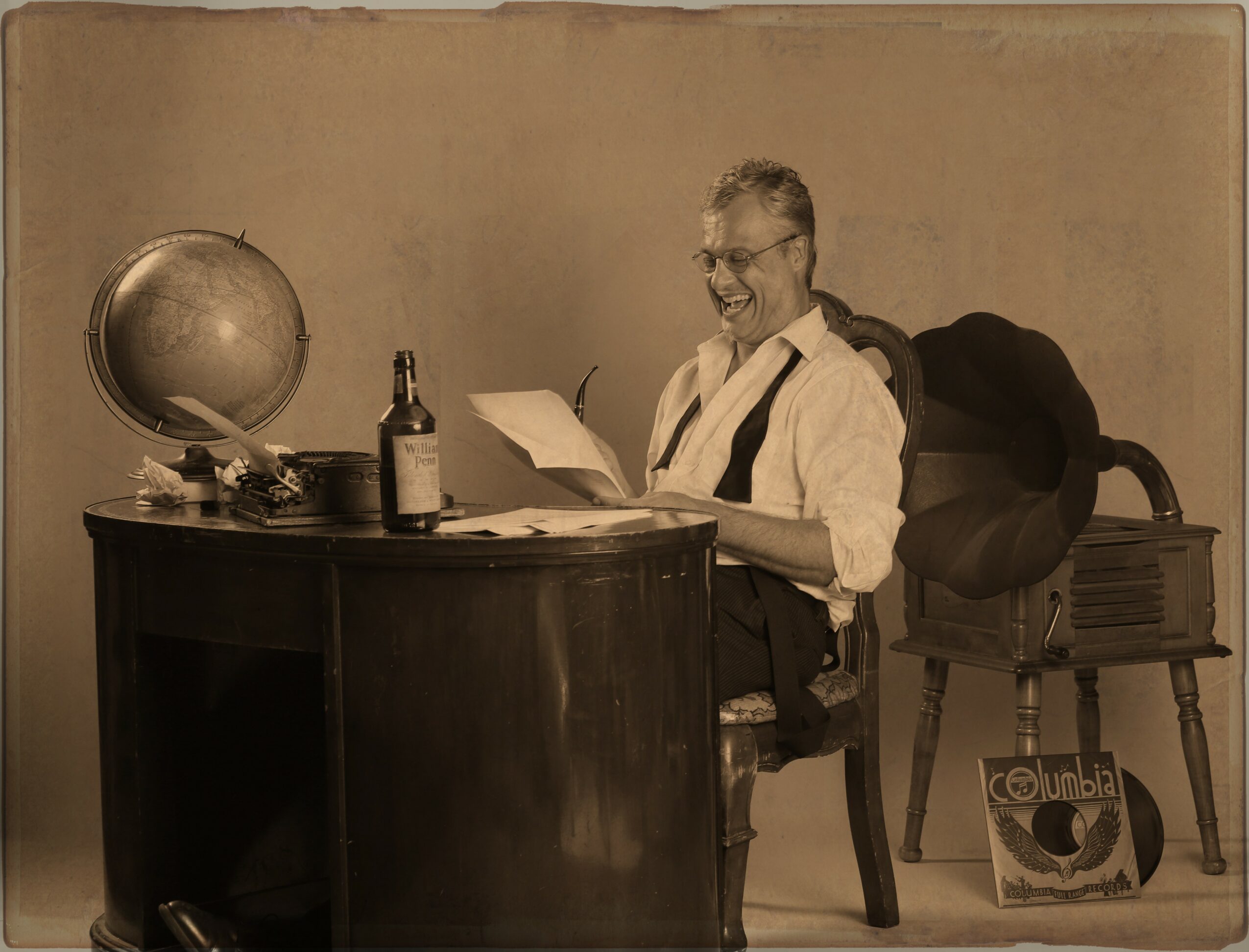 Man sitting at desk reading a book, with a globe, bottle, and papers, in a vintage office setting.