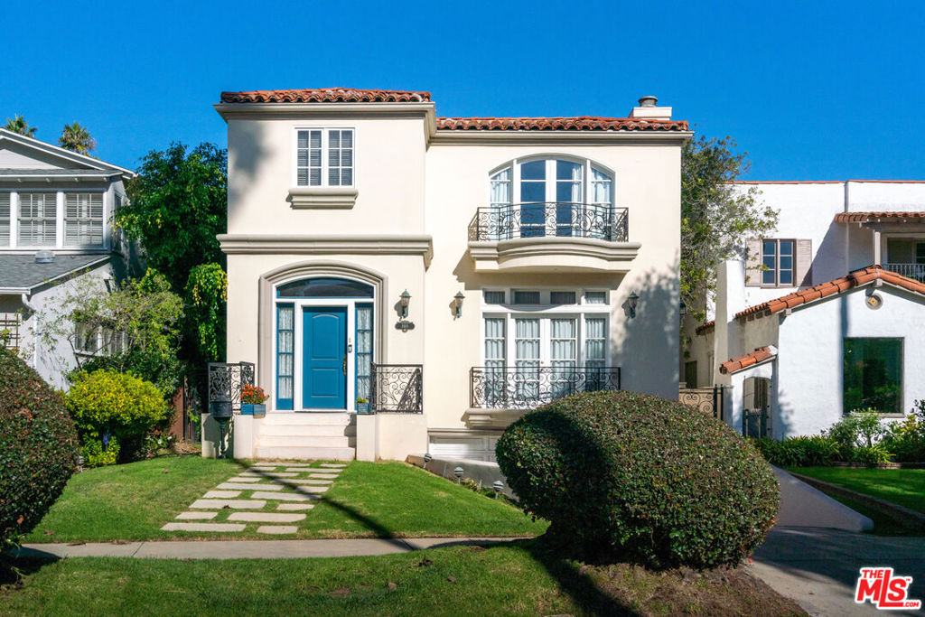 Two-story house with a blue front door, balcony, and well-maintained lawn, under a clear blue sky.