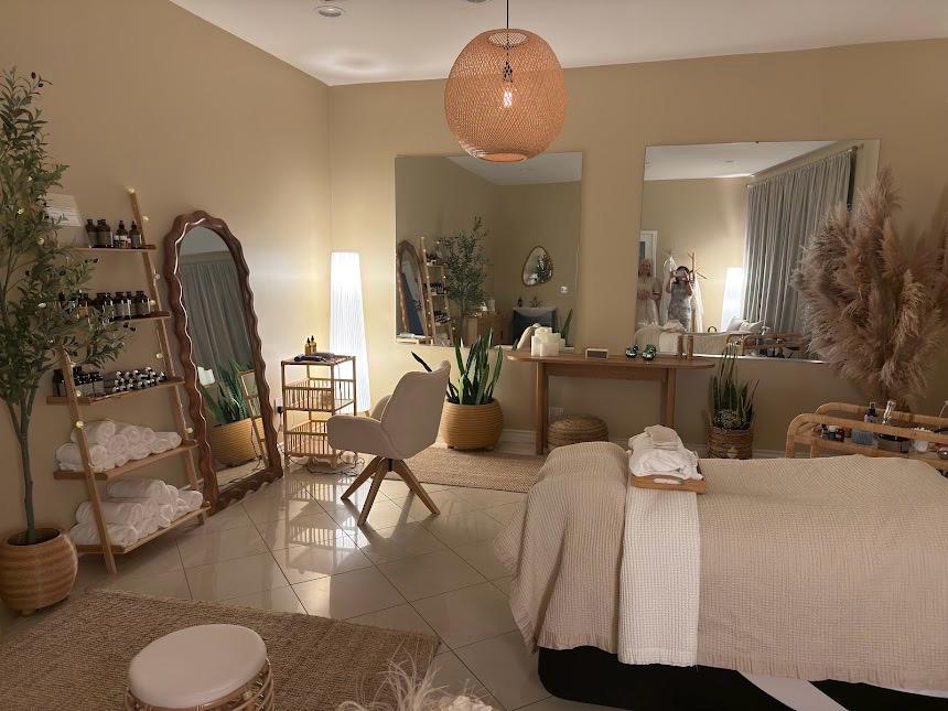 Living room with a mirror, lamp, chair, plants, and a bed with white linens, in a cozy space.