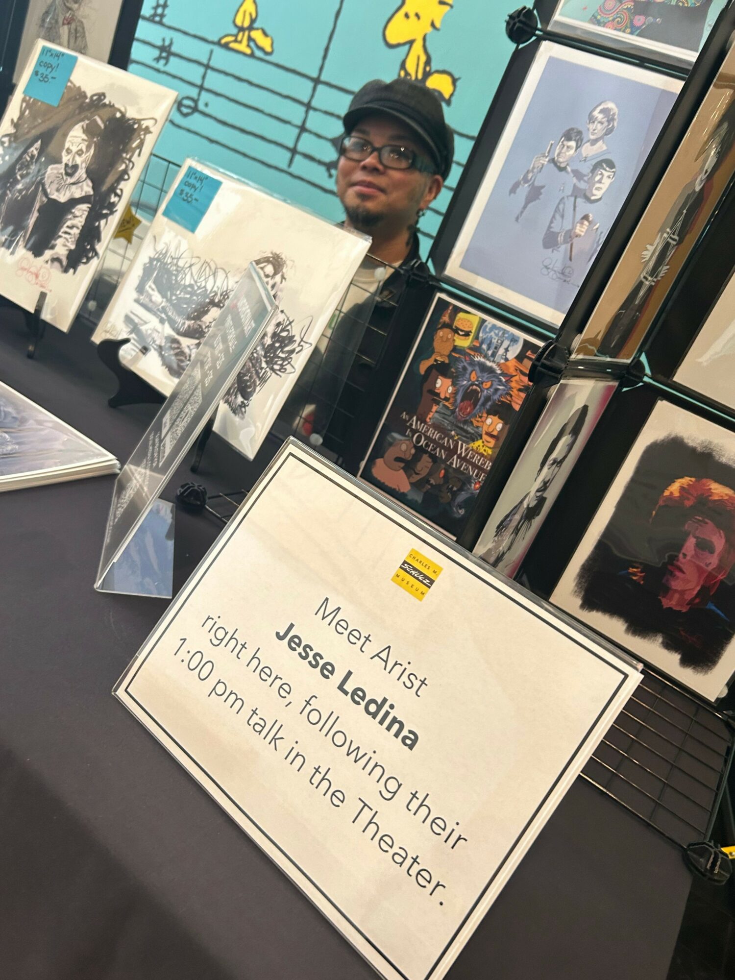 Display table with artwork and a sign about artist Jesse Ledina's talk at the theater.
