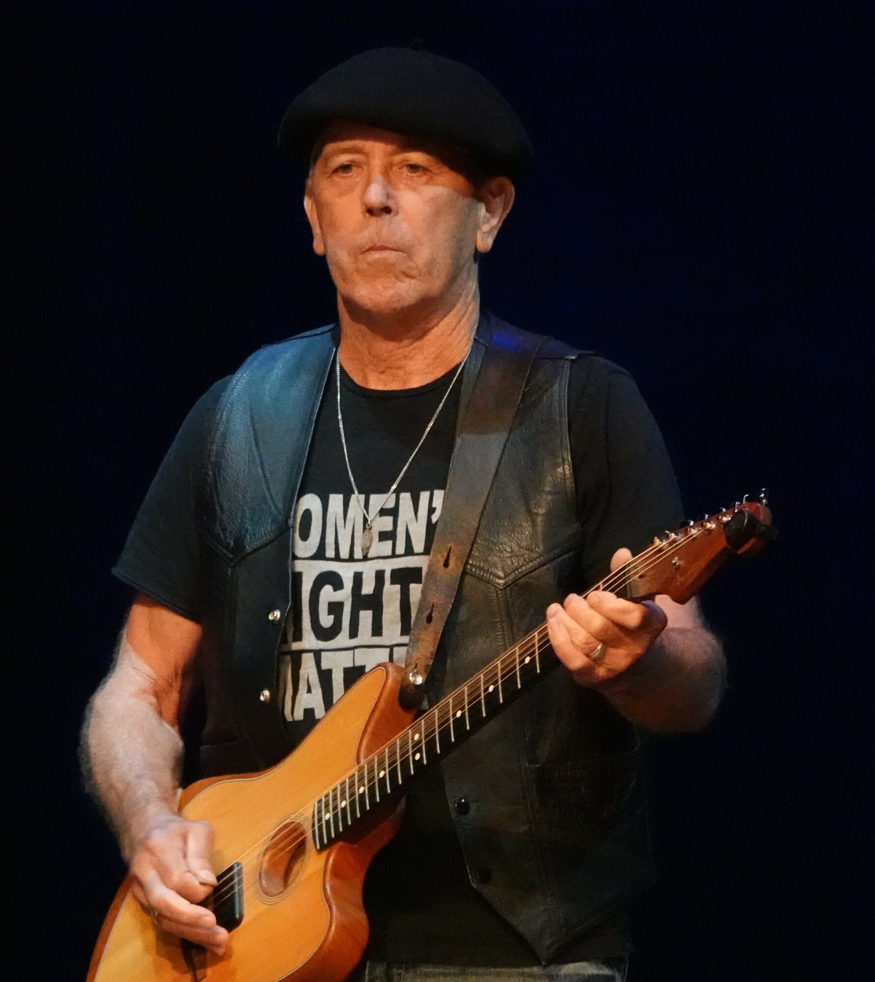 Man wearing a black hat and T-shirt playing an electric guitar on stage.