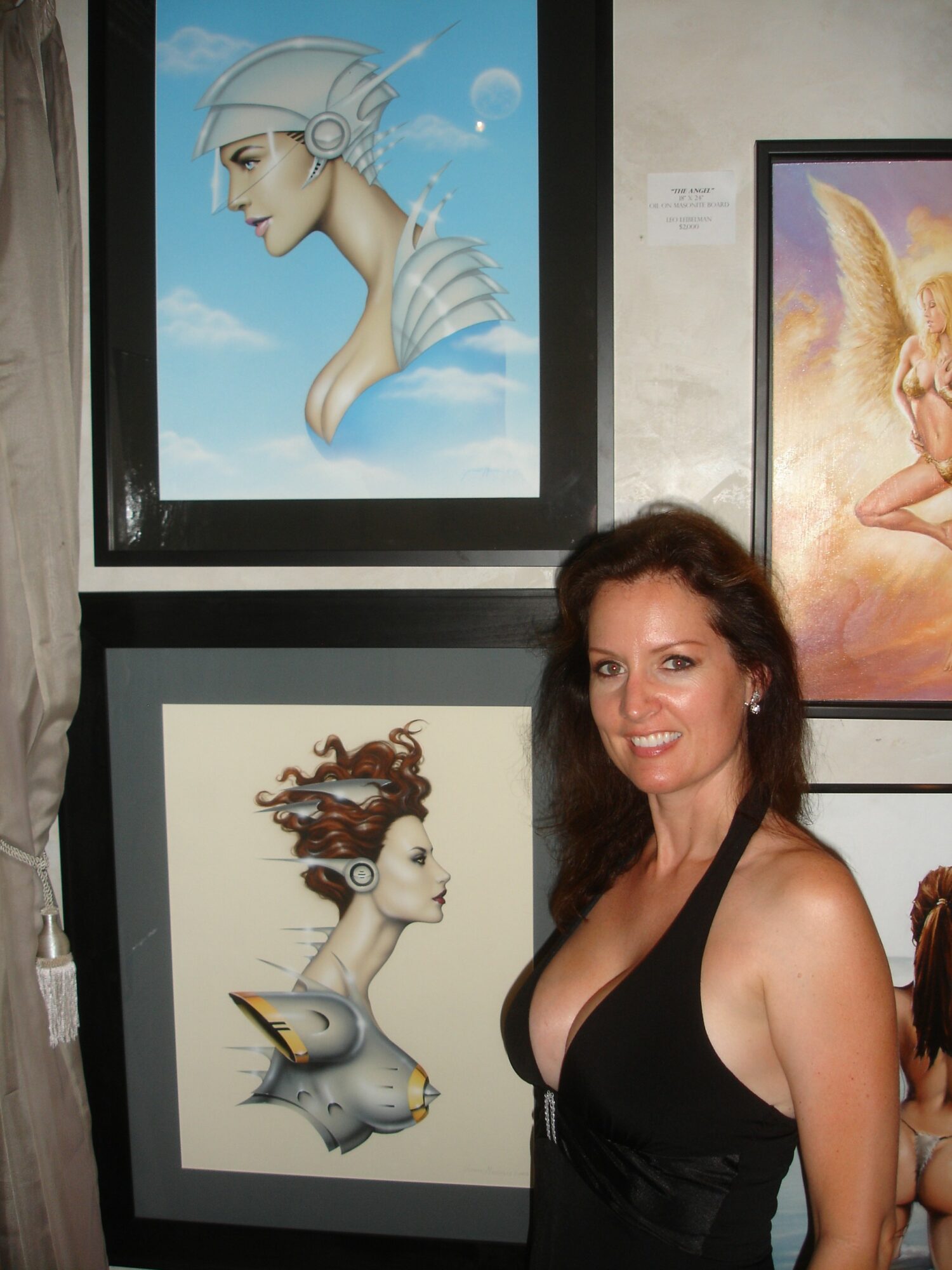 Woman with dark hair in a black dress standing in front of framed artwork, smiling at the camera.