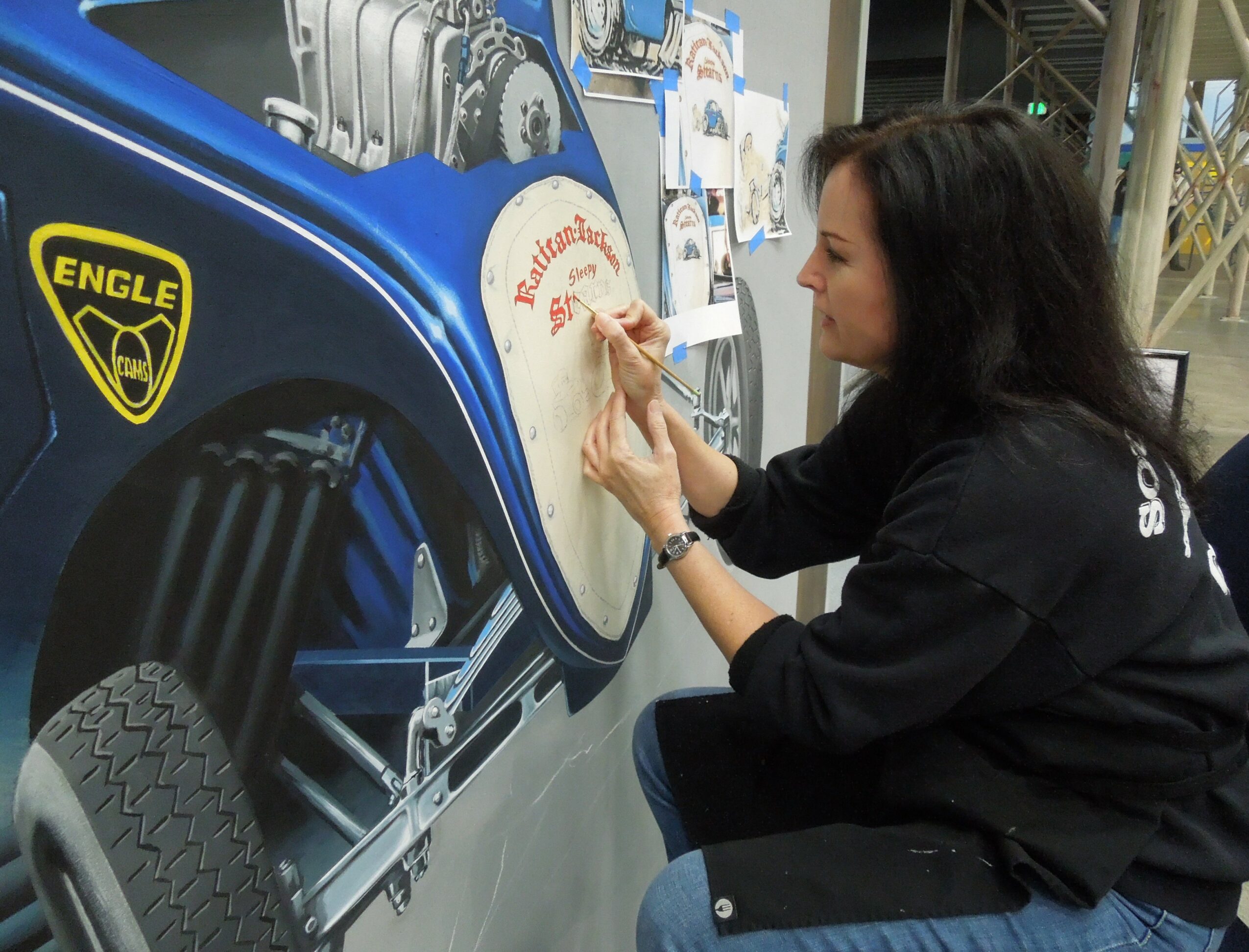 Woman writing on a circular sign at a mechanical-themed display with a blue background and a yellow logo.