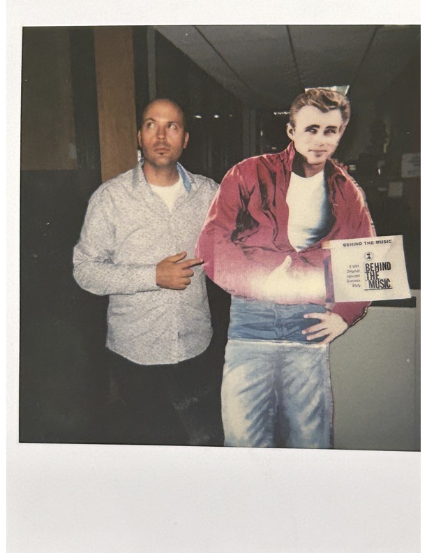 Person standing next to a life-sized cutout of a man holding a sign, in an indoor setting.