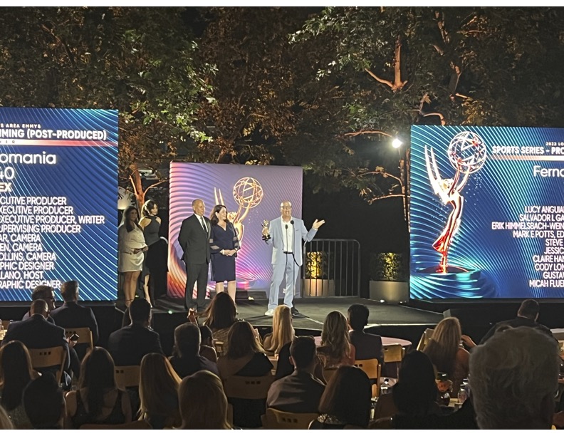 People on stage at an awards event with large screens displaying text and graphics, audience watching outdoors at night.