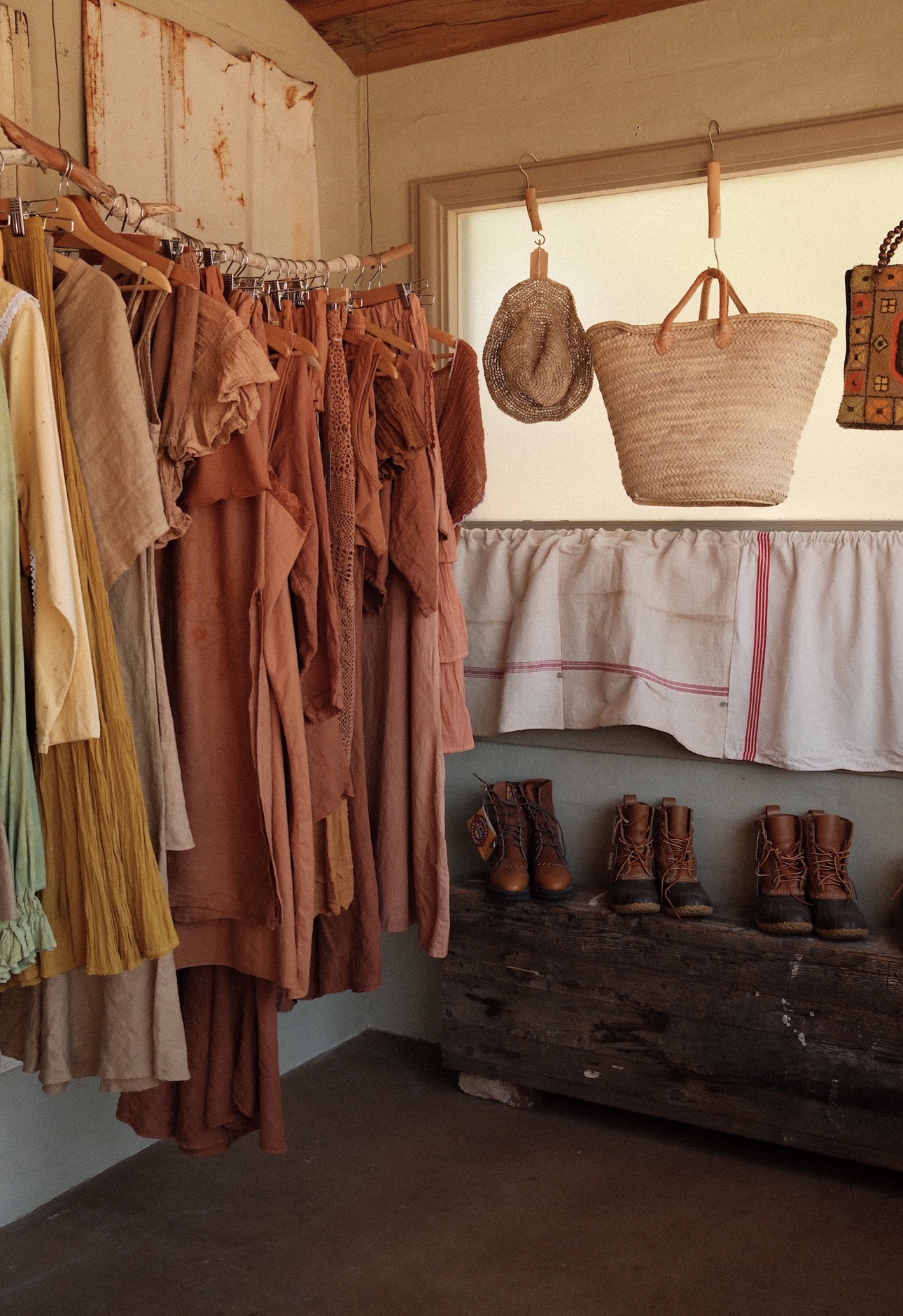 Clothes hanging on a rack, baskets, and boots on a wooden surface inside a rustic room.