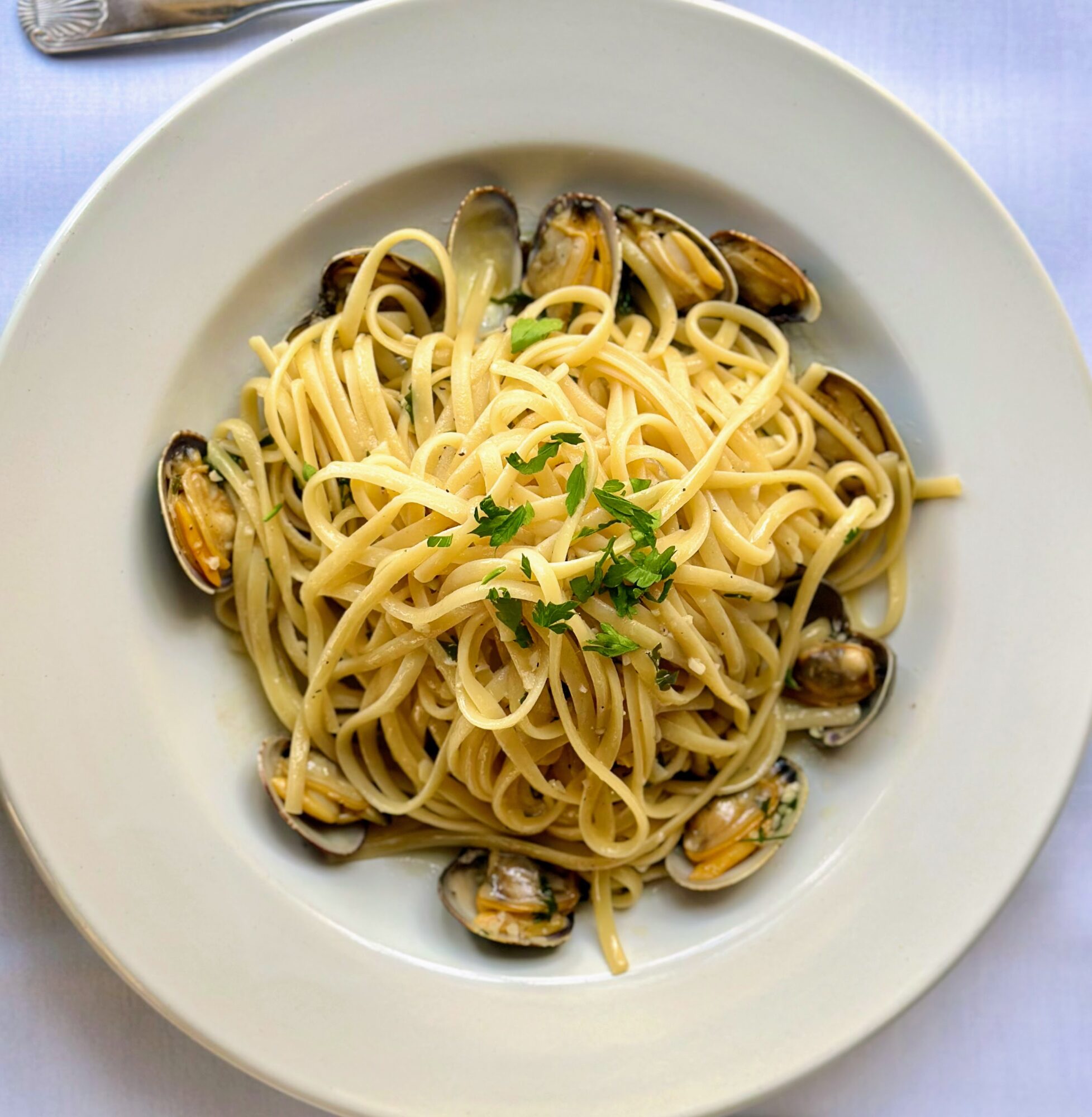 Plate of spaghetti with clams garnished with parsley, on a white tablecloth