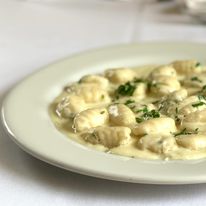 Creamy soup with dumplings and herbs in a white bowl on a white surface.