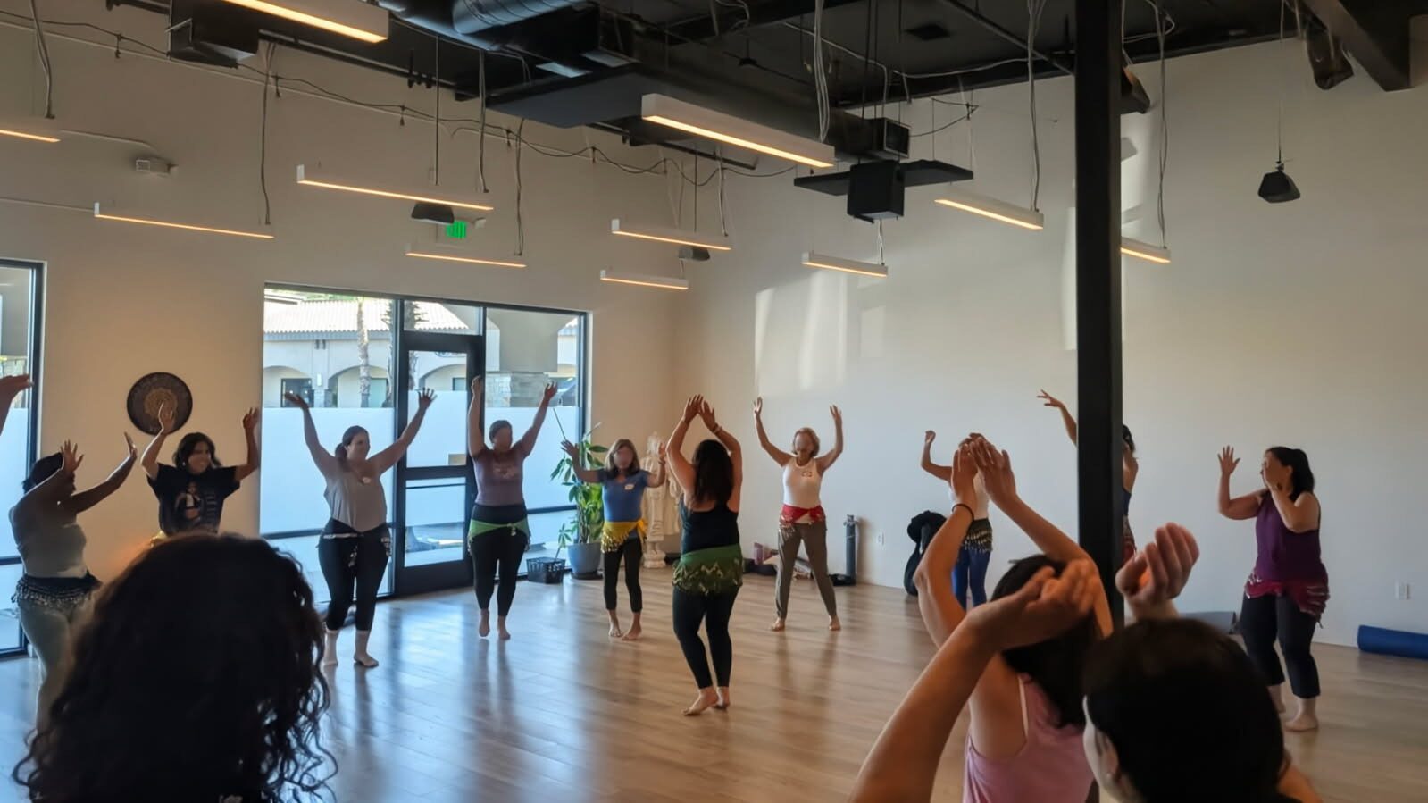 Group of people participating in a dance or exercise class in a spacious studio with large windows and wooden floor.