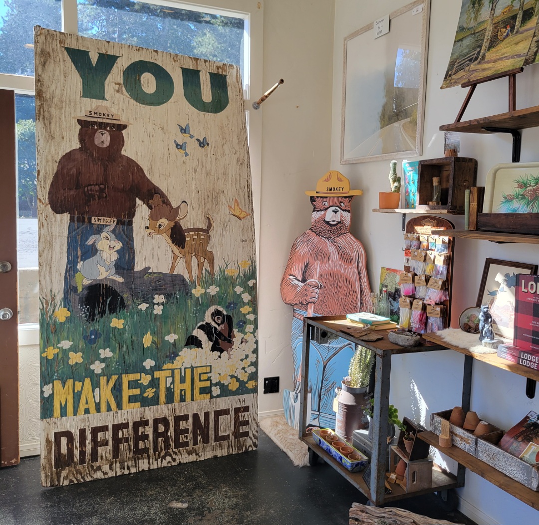 Art display with a bear, dog, and cat, and the words 'You Make the Difference' on a wooden panel, in a room with shelves and artwork.