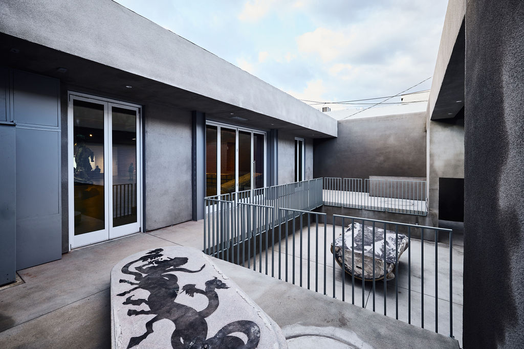 Outdoor balcony with railing, a decorative rug with a dragon design, and a stone sculpture, against a modern building background.