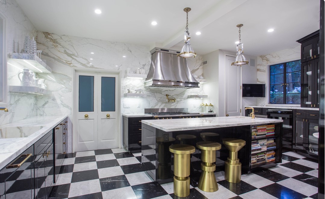 Modern kitchen with black and white checkered floor, marble walls, island with gold stools, and stainless steel appliances.