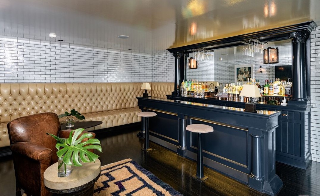 Bar area with a dark blue counter, beige tufted seating, a leather chair, and a small table with a plant.