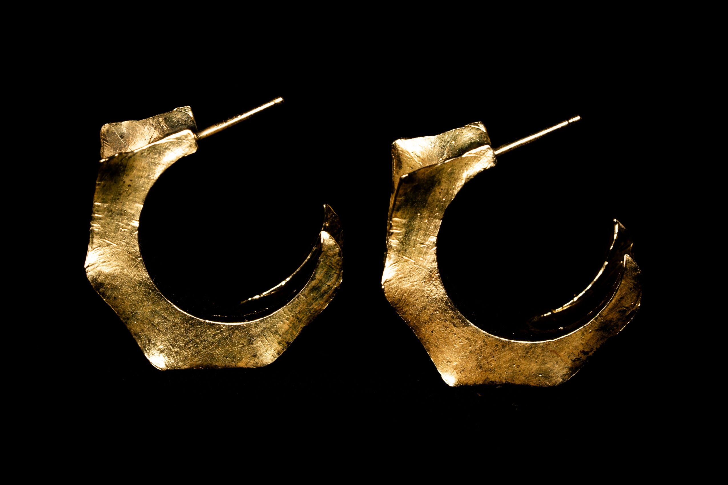 Gold-colored hoop earrings with a textured surface, set against a black background.
