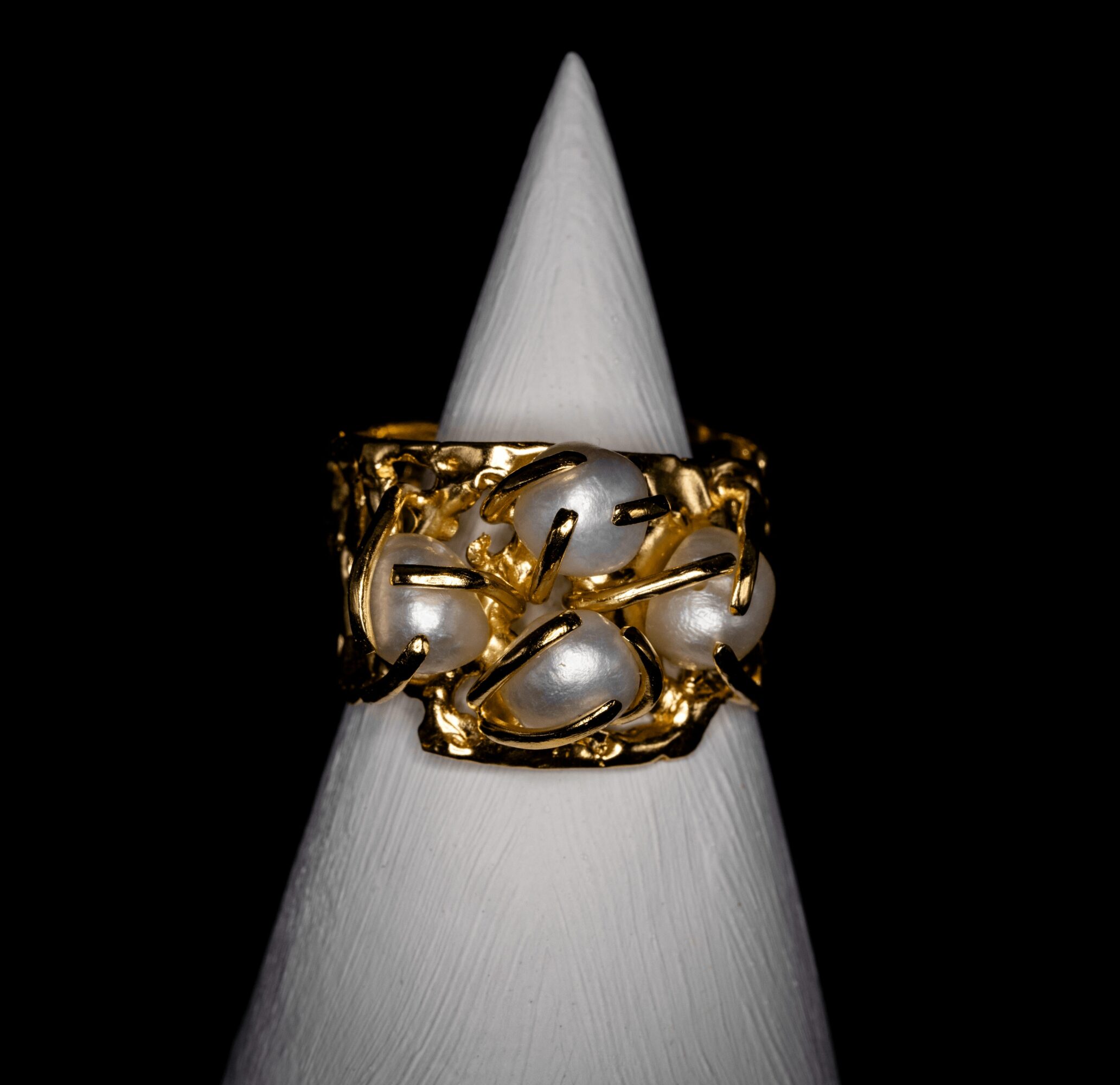 Ring with gold and pearl design displayed on a white cone against a black background.