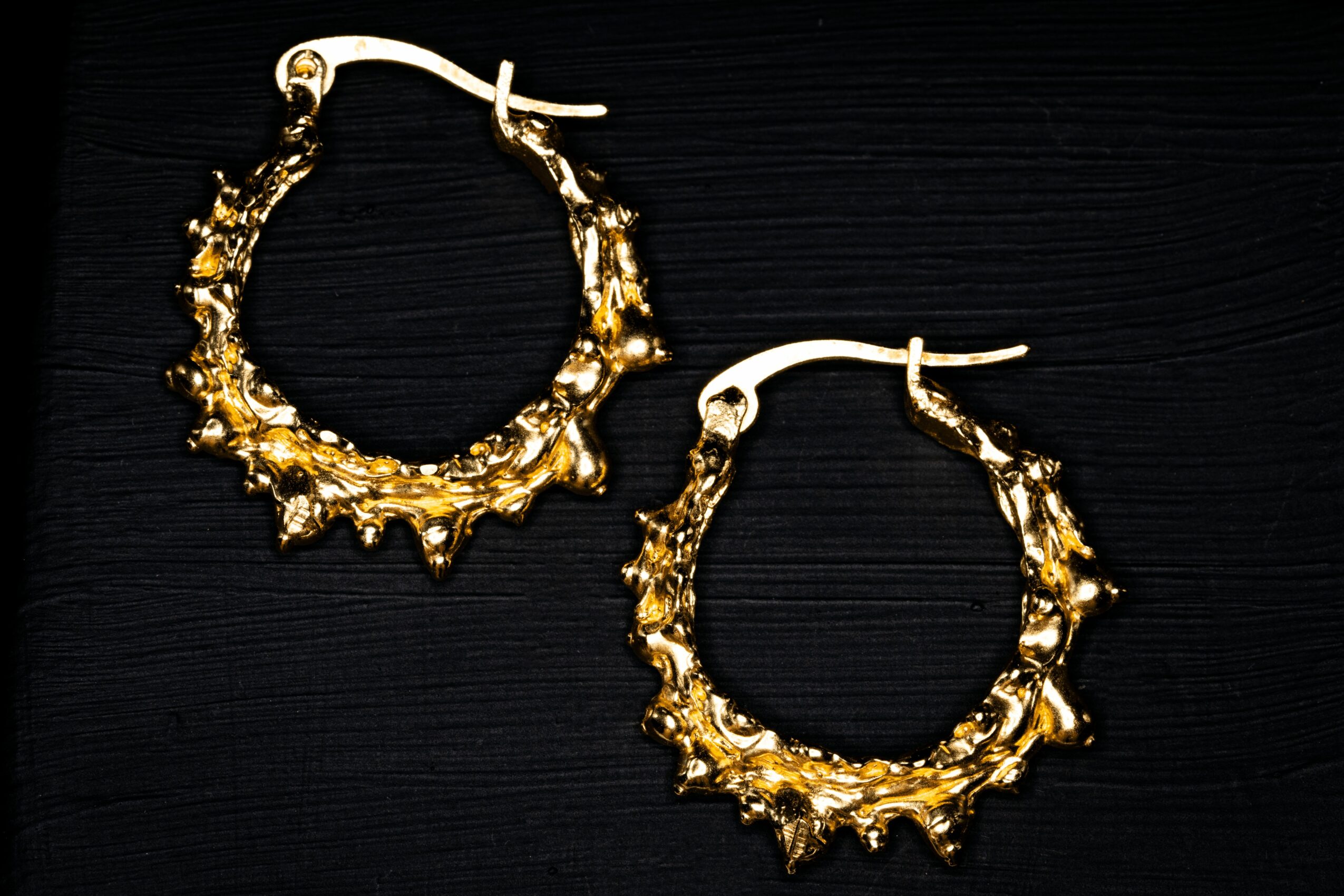 Pair of gold hoop earrings with jagged, textured design on a black background.