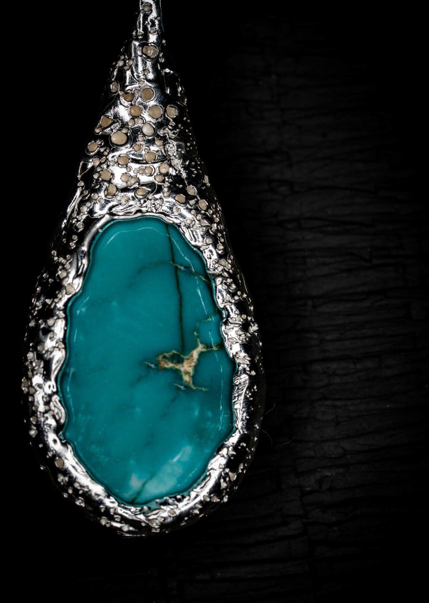 Teardrop-shaped turquoise gemstone pendant with silver setting, hanging against a black background.