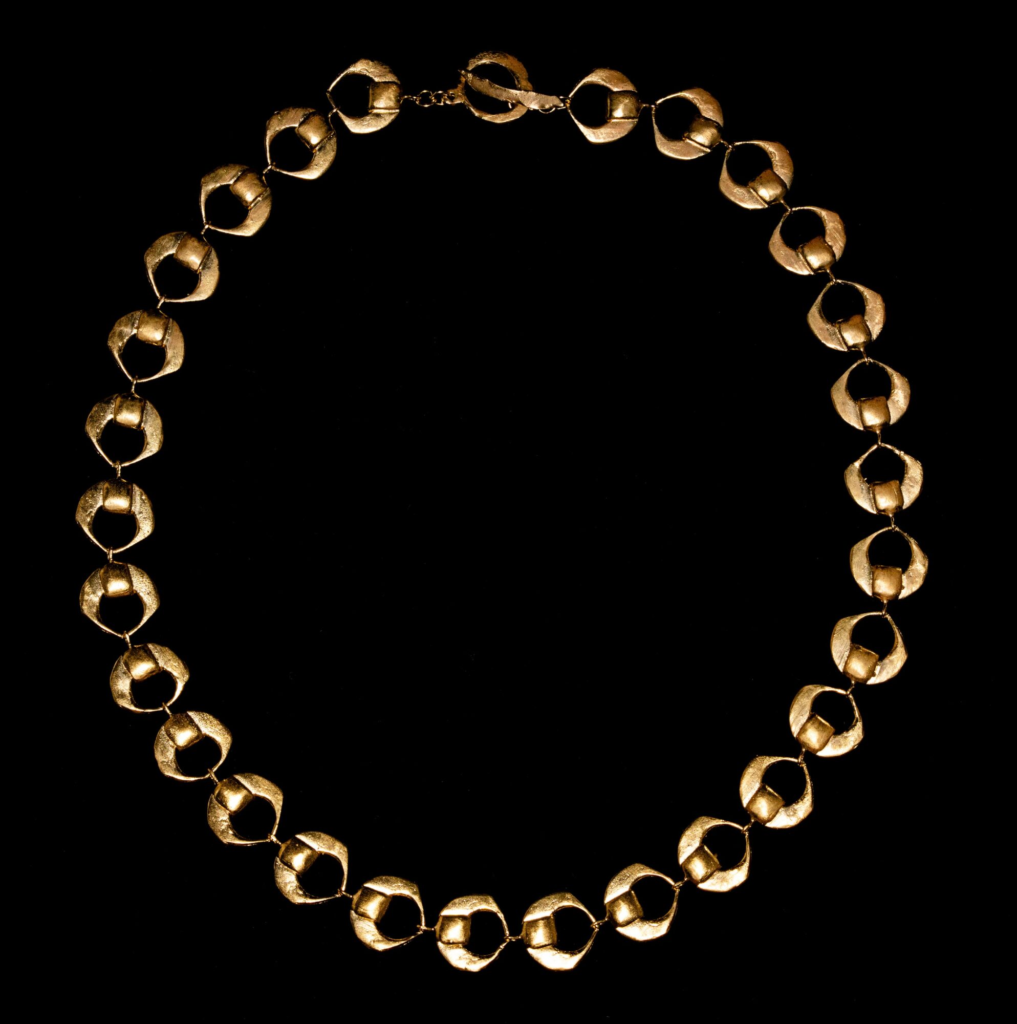 Gold-colored beaded necklace arranged in a circle on a black background.