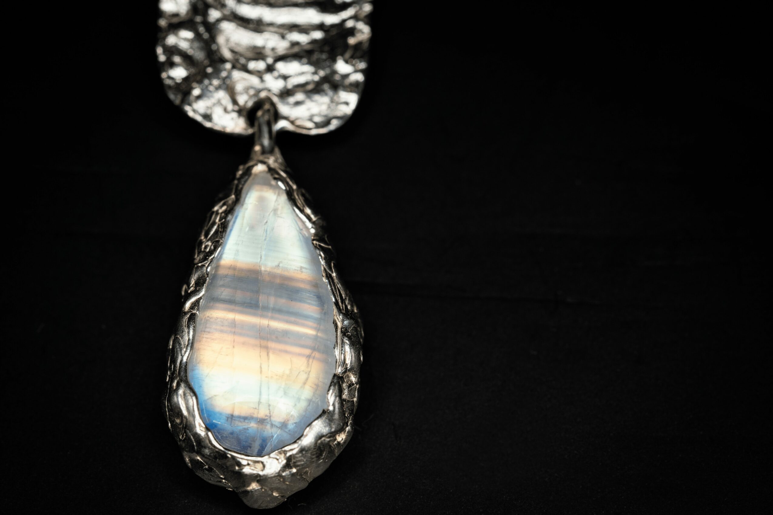 Pendant with a teardrop-shaped, iridescent stone in a decorative metal setting against a black background.