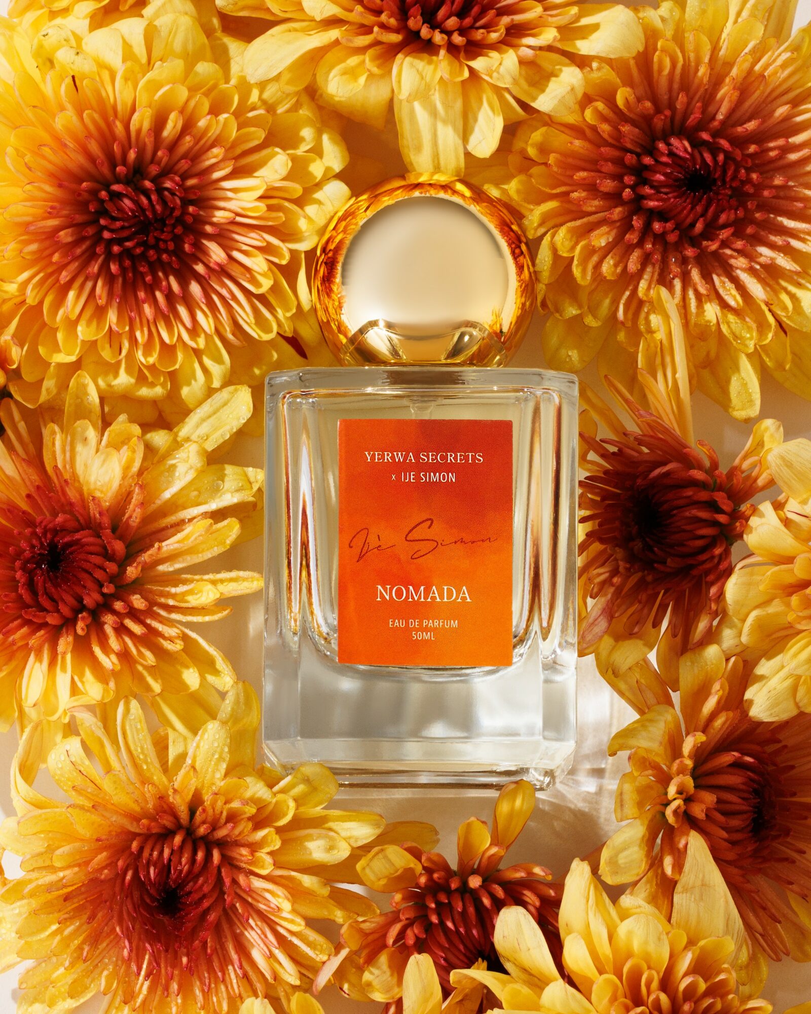 Perfume bottle surrounded by yellow and orange flowers, with a pink label and gold cap.