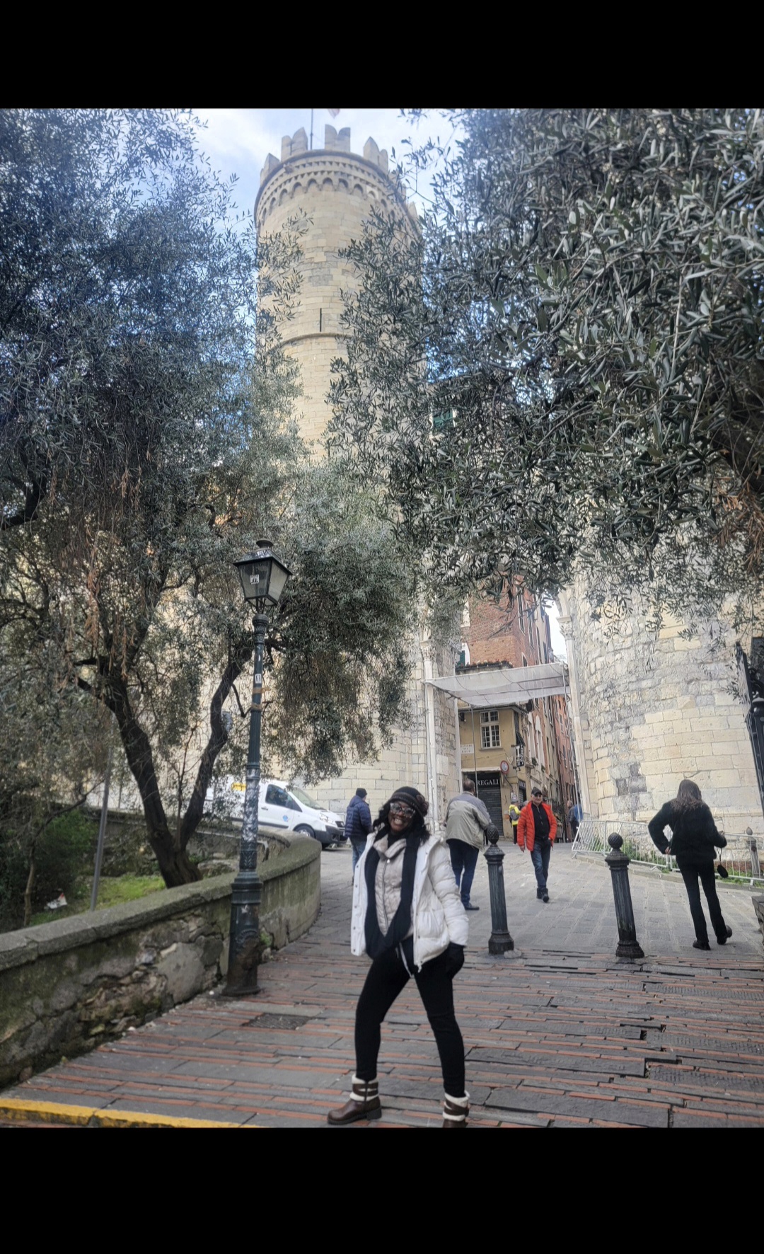 Person standing on a paved path with trees and a tower in the background.