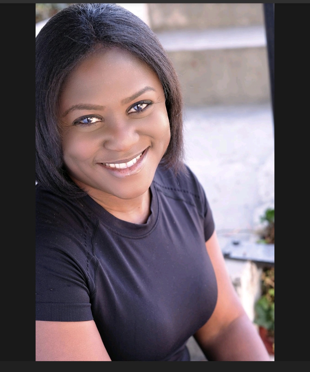 Smiling woman with dark hair wearing a black shirt outdoors, steps in the background.