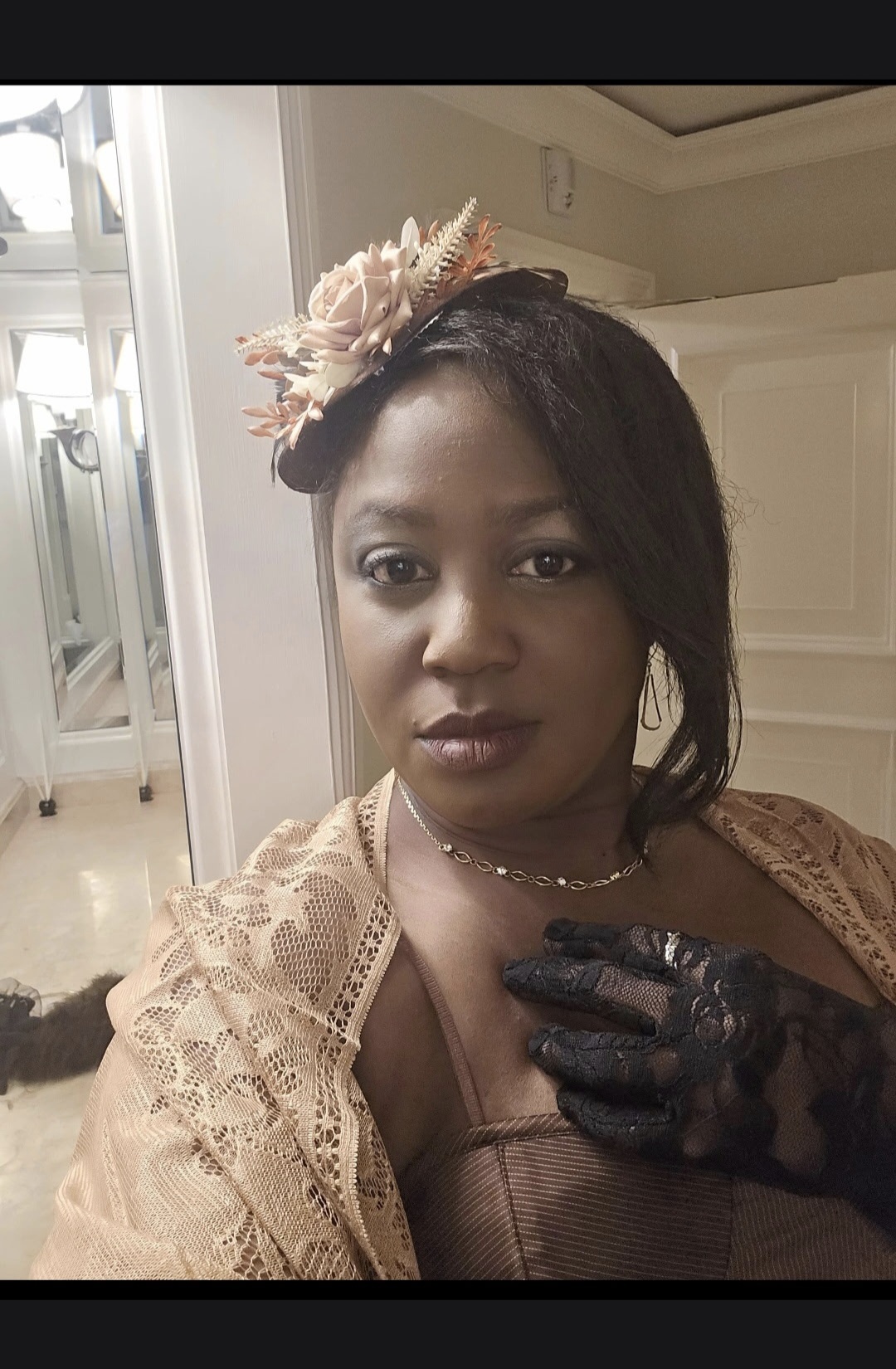 Woman with floral headpiece and lace shawl, looking at camera indoors, with a hand in black glove near her chest.