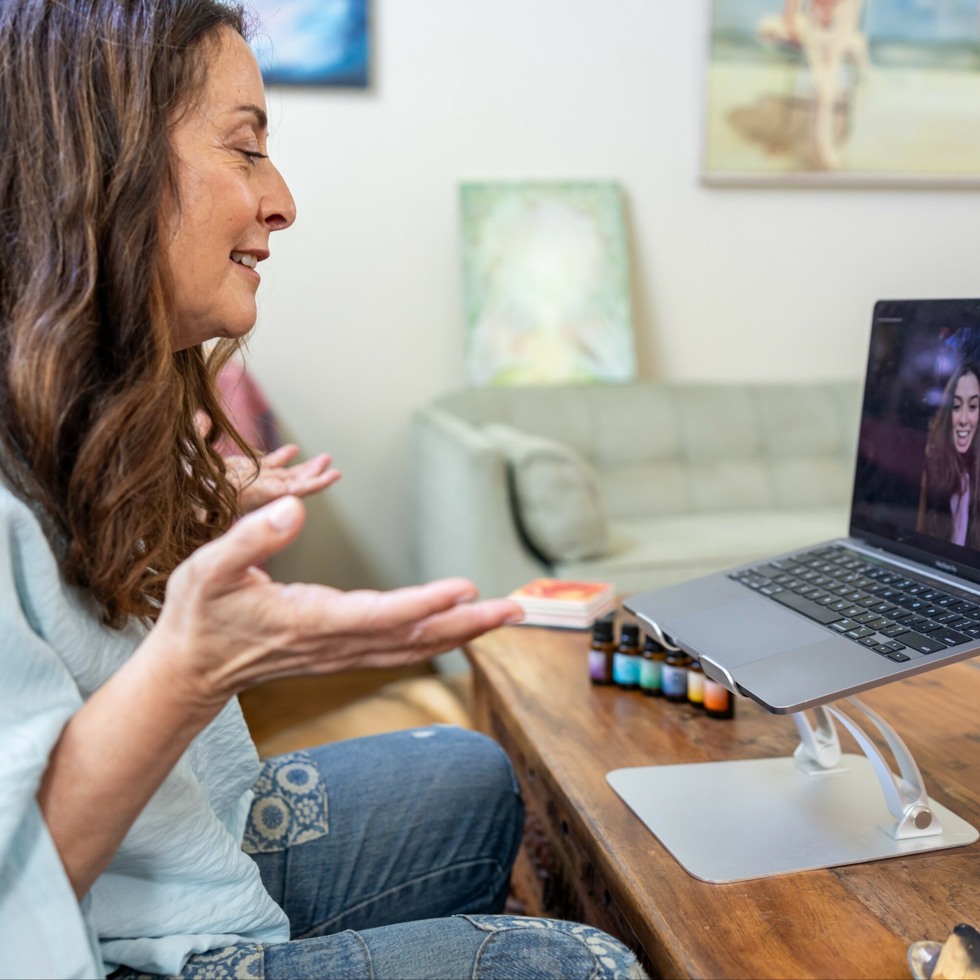 Woman engaging in a video call on a laptop, gesturing with her hands, in a cozy living room setting.