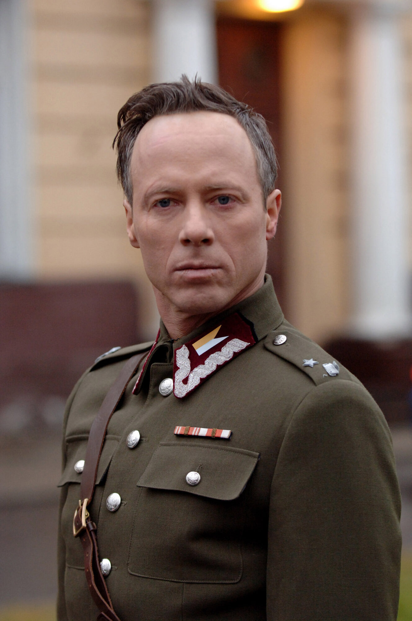 Man in military uniform with medals and insignia, standing outdoors with blurred background.