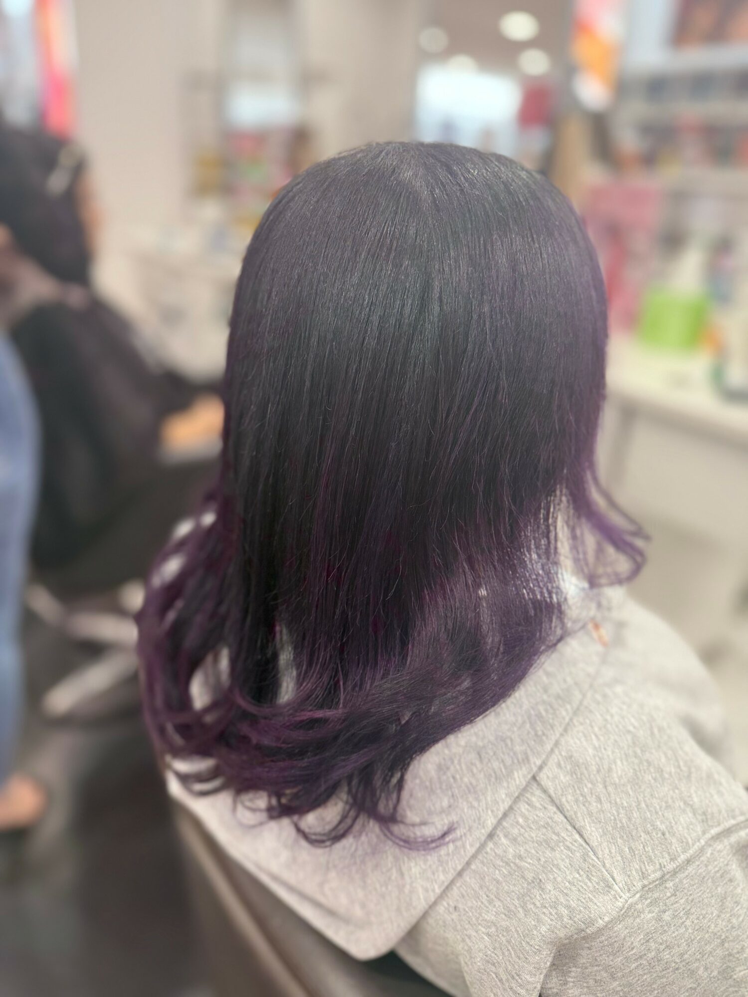 Person with black hair fading to purple at the ends, sitting in a store or salon, facing away from the camera.