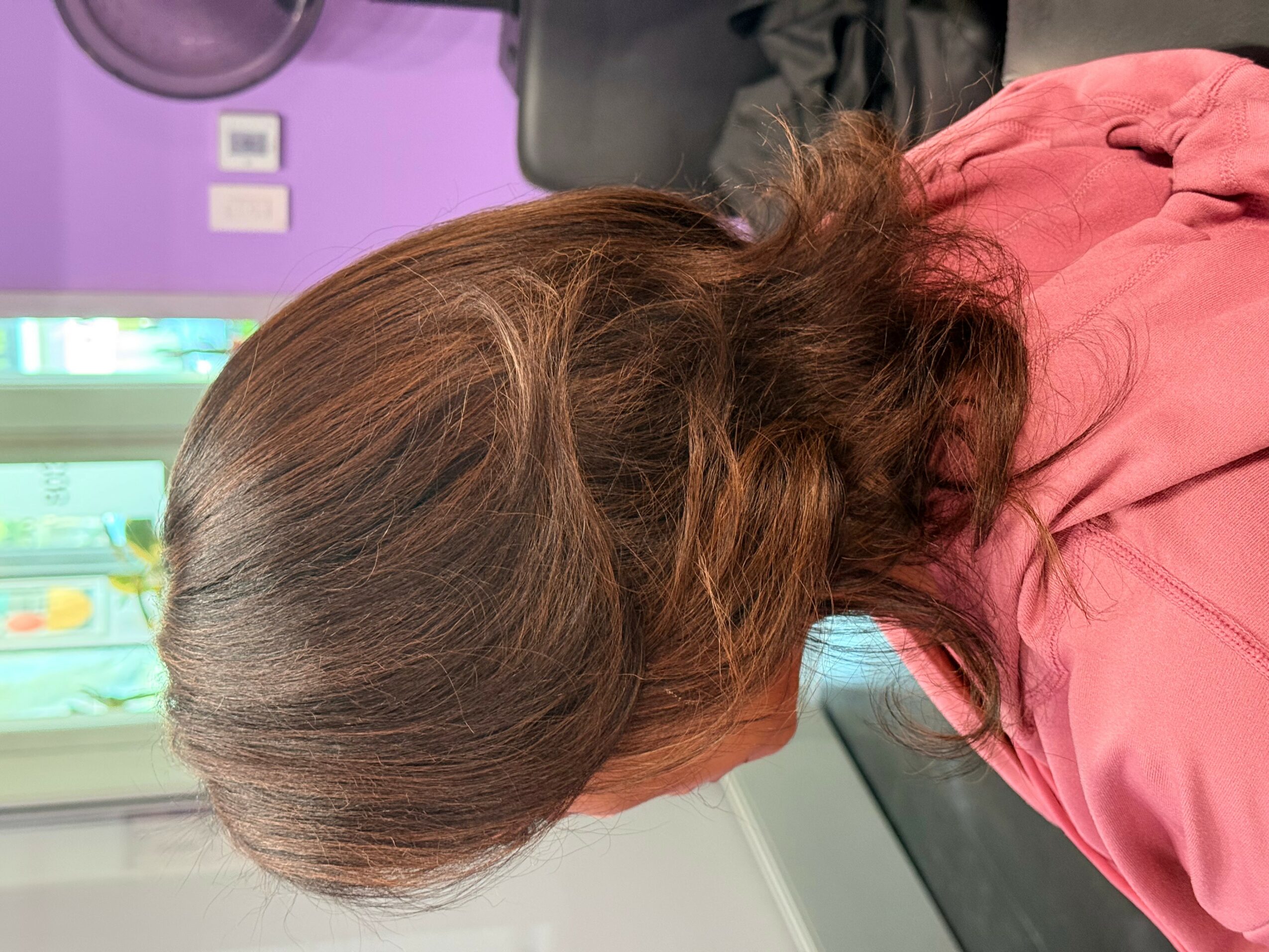 Side view of a woman with brown hair, wearing a pink top, in a room with purple walls and a window.