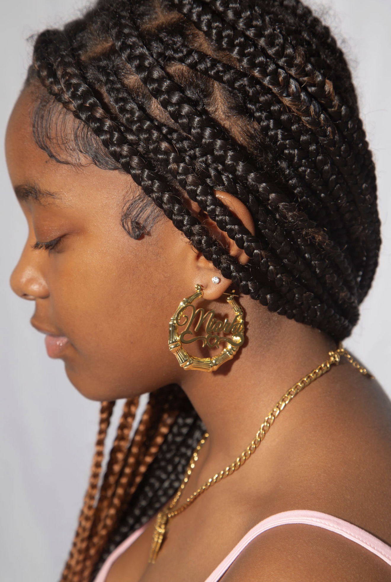 Side profile of a woman with braided hair, wearing large hoop earrings and a gold necklace.